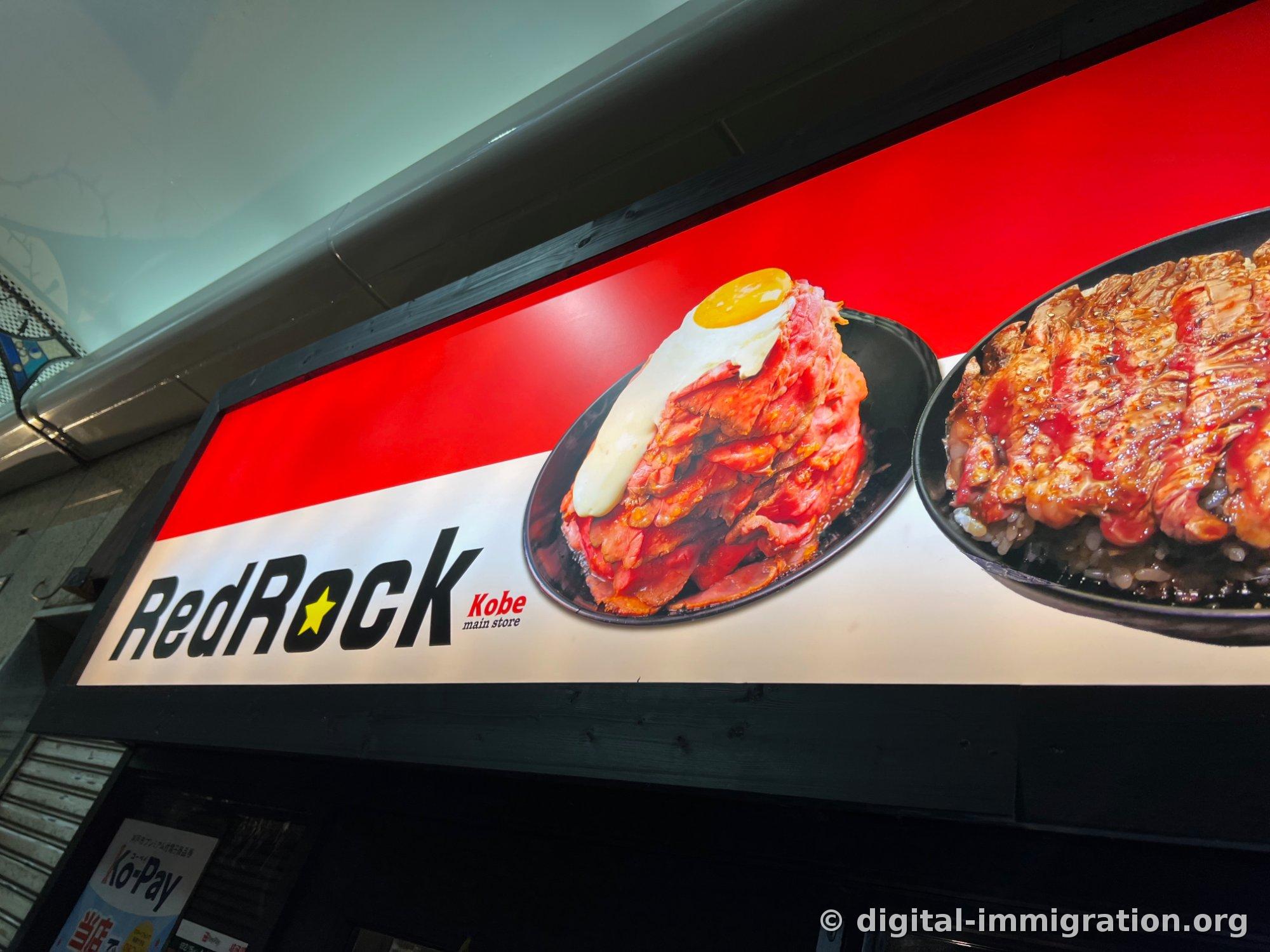 Une enseigne de restaurant affichant le logo 'RedRock Kobe main store' sur fond rouge avec des photos de roast beef donburi garni d'un jaune d'œuf et de steak donburi grillé