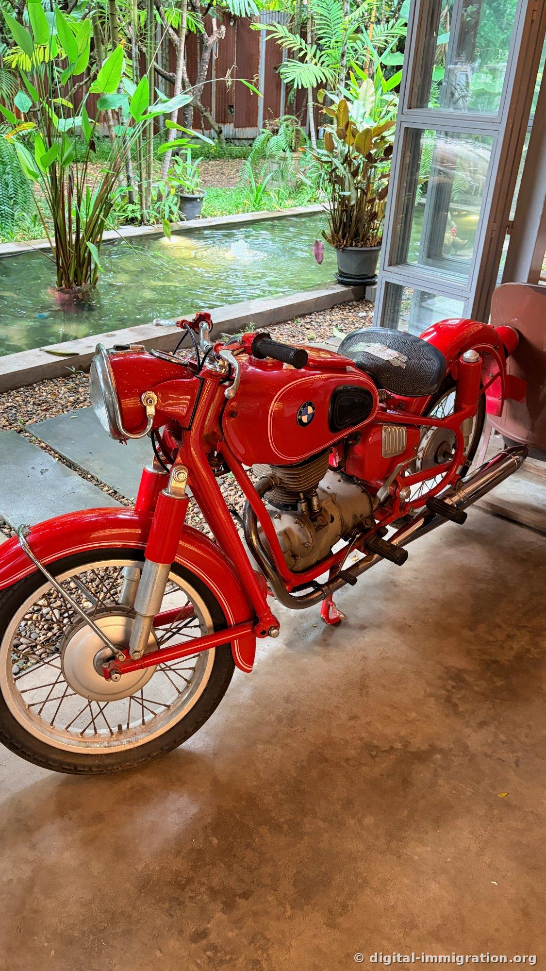 Une moto BMW classique rouge garée sur le sol en ciment à côté d'une pièce d'eau, le phare chromé et le silencieux brillent