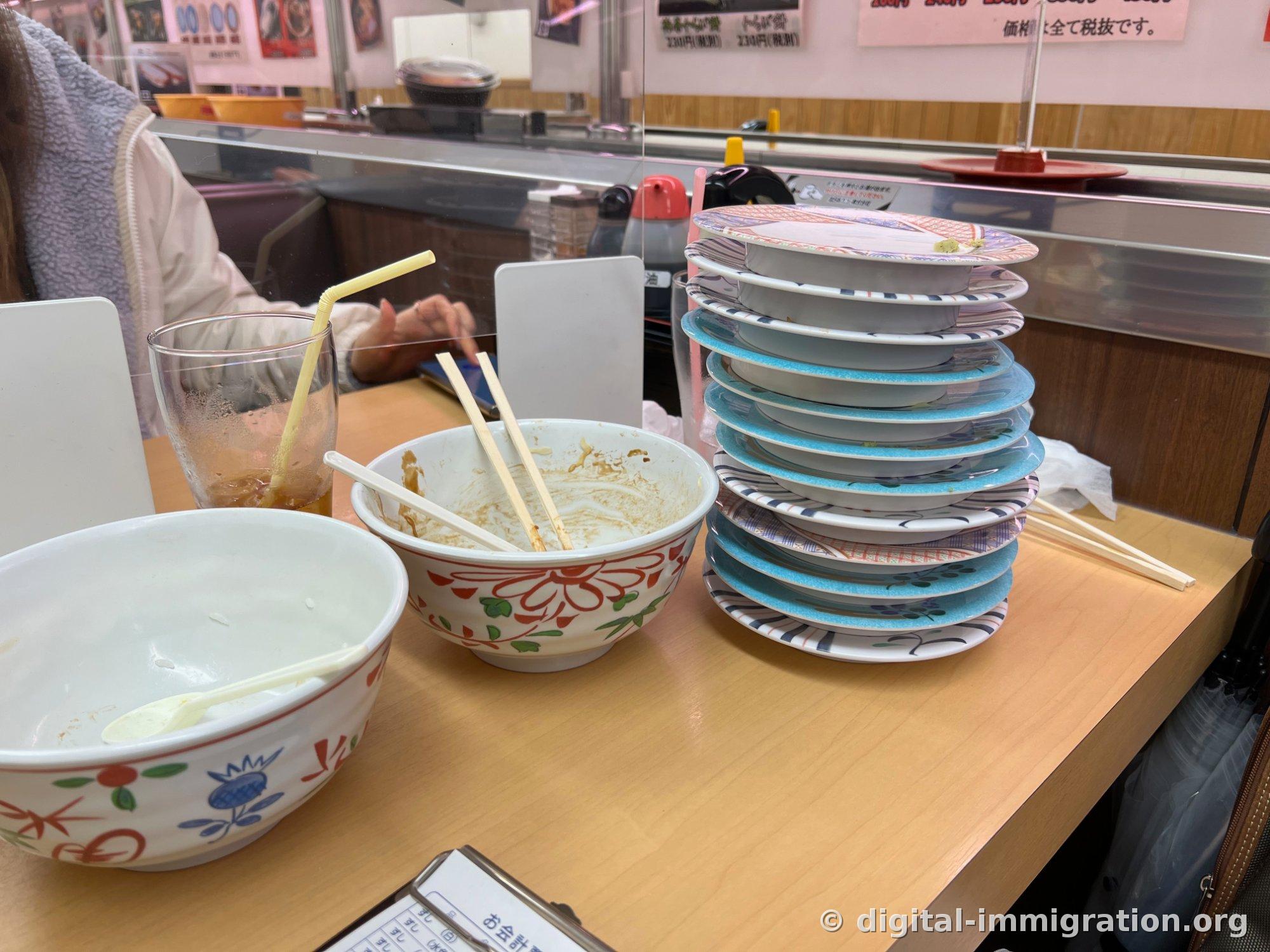 吃完饭后转盘寿司柜台上按颜色堆起的十二个空盘子、还有汤的碗和账单