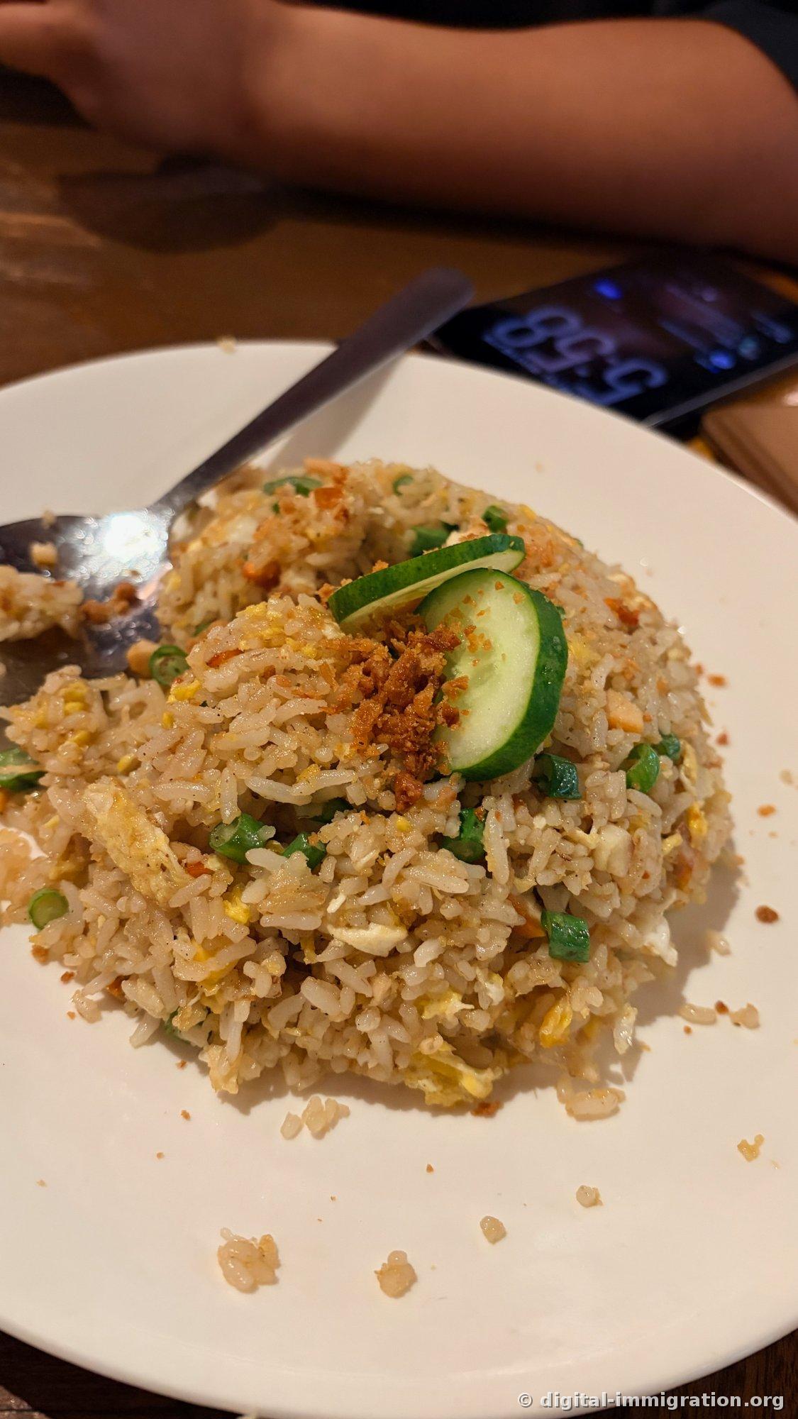 Fried rice with egg and scallions, topped with crispy fried garlic, two cucumber slices, and a lime wedge on a white plate