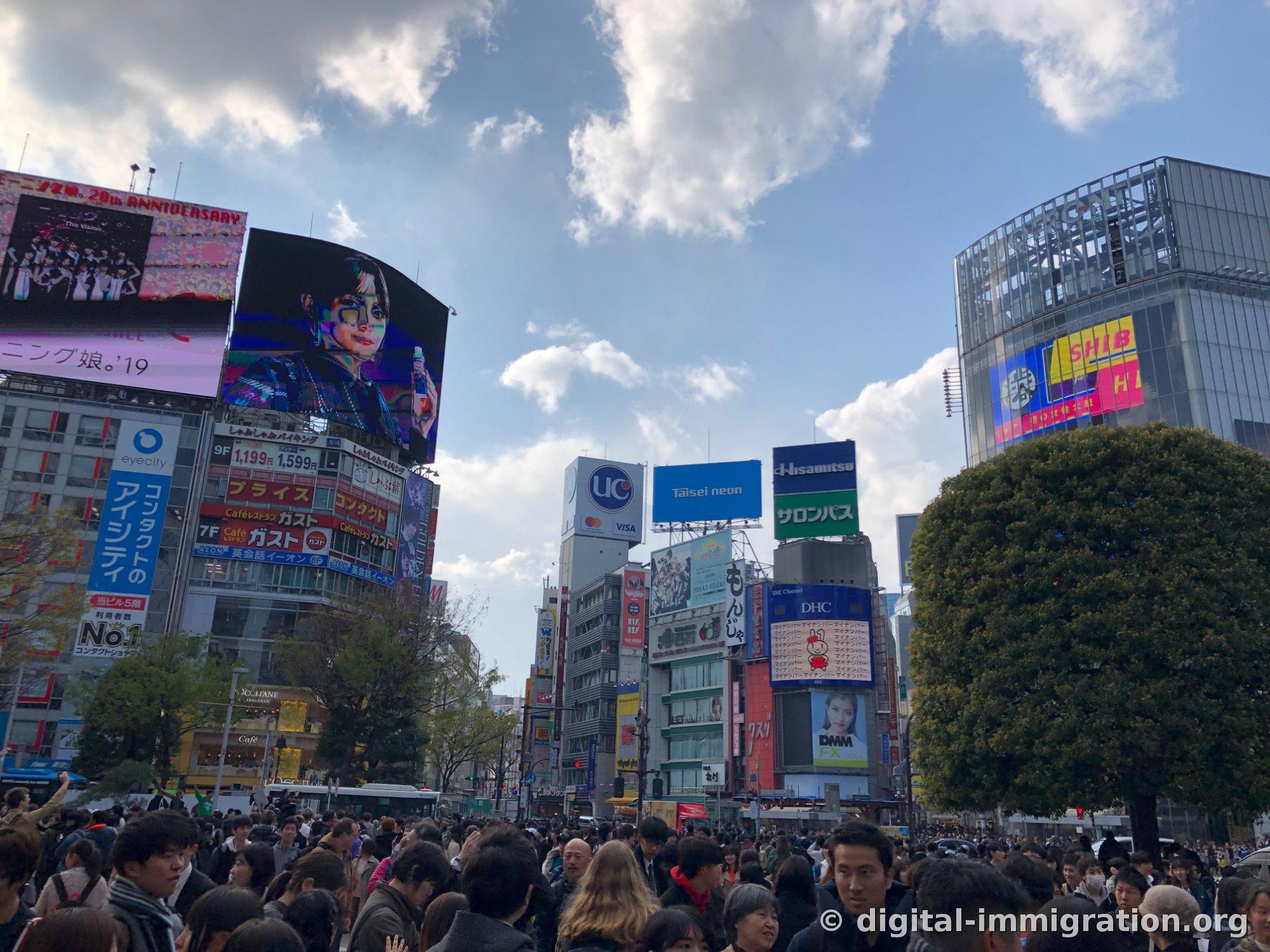 昼の渋谷スクランブル交差点、青い空の下に大型広告板としゃぶしゃぶバイキング1,199円の看板、下は人混みでいっぱい