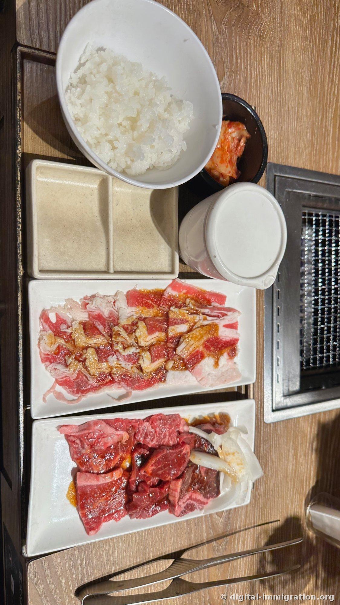 Vue de haut de la table. Riz blanc, kimchi, verre d'eau, une assiette de viande mince marinée, et une assiette de bavette épaisse accompagnée d'oignons