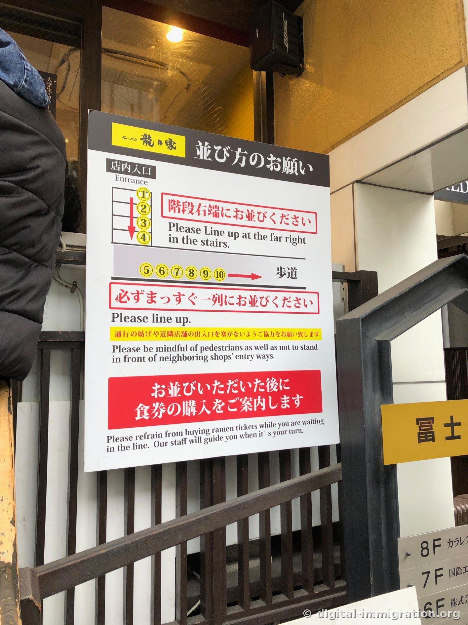 Panneau d'information en japonais et en anglais montrant comment faire la queue : 1-4 à droite de l'escalier, 5-10 sur le trottoir