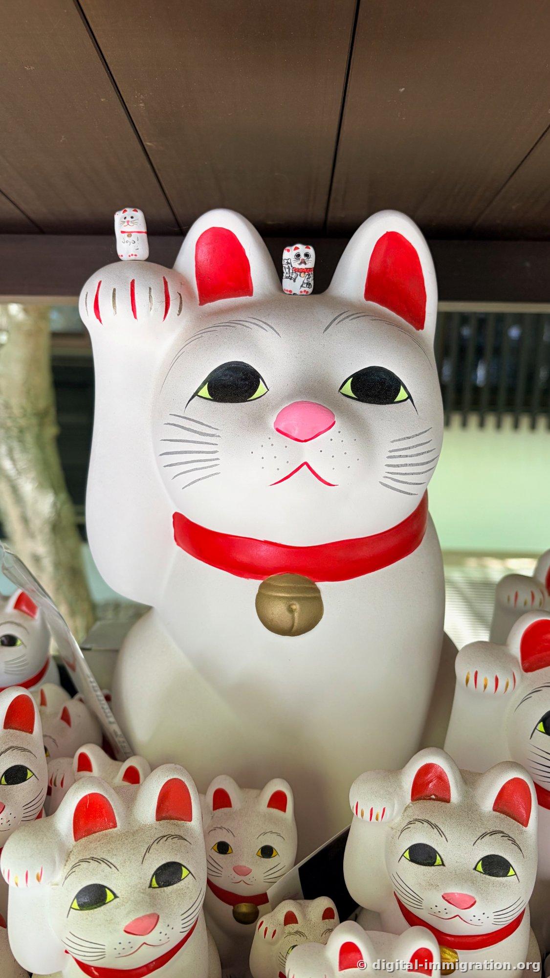 Two tiny cat figurines placed on the head and raised paw of a large white beckoning cat