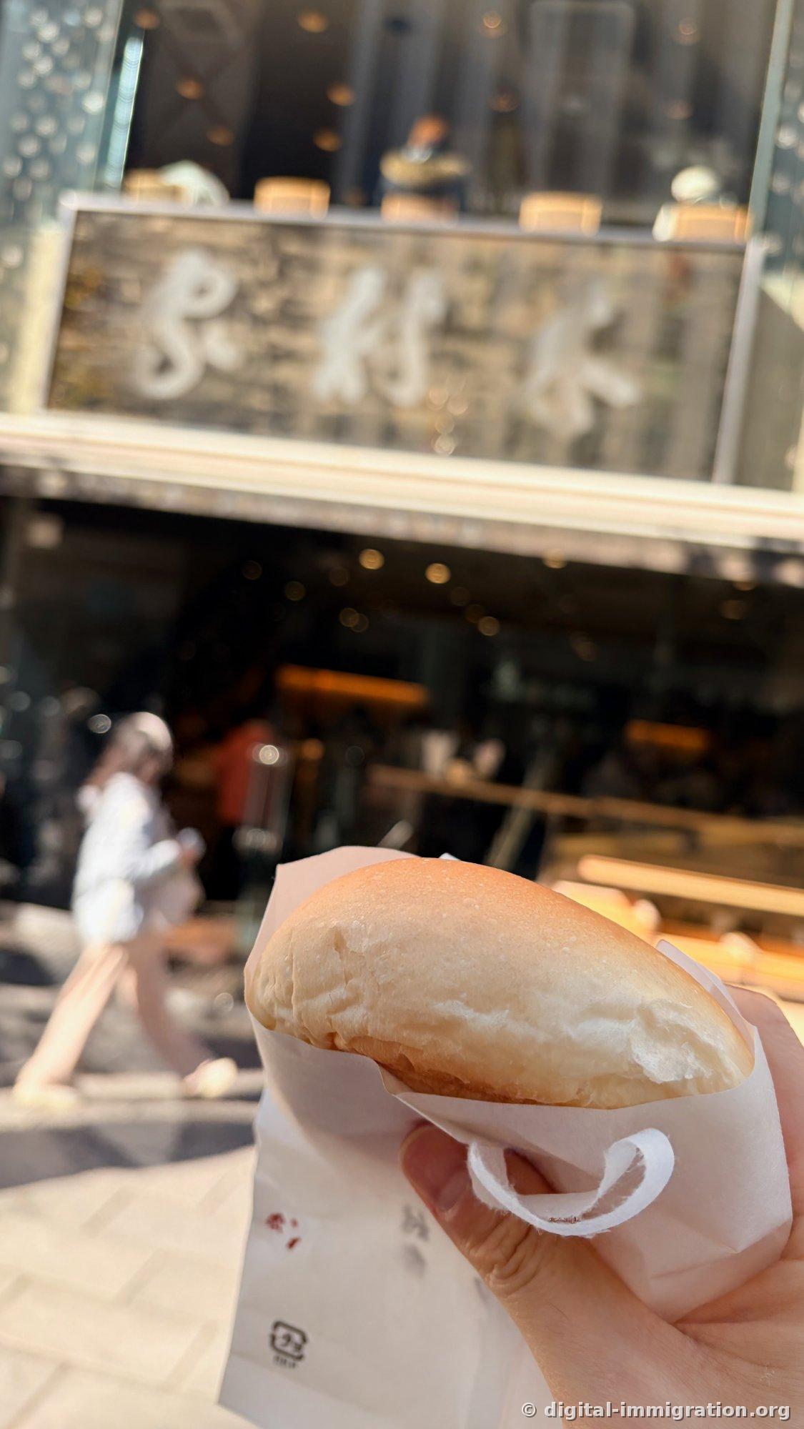 Wrapped round anpan held in hand with Kimuraya wooden signboard in background