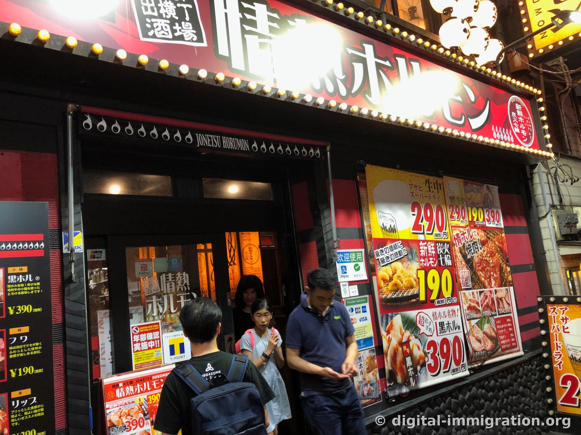 Des clients qui attendent devant le restaurant et une affiche de fenêtre indiquant les prix 190 yen, 290 yen, 390 yen