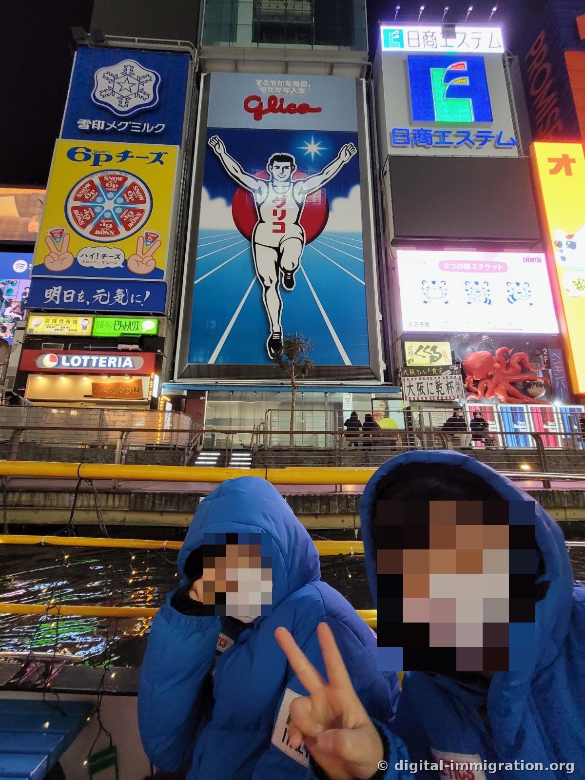 Deux enfants en duvet bleu posant avec le signe V devant l'enseigne Glico depuis le bateau de croisière