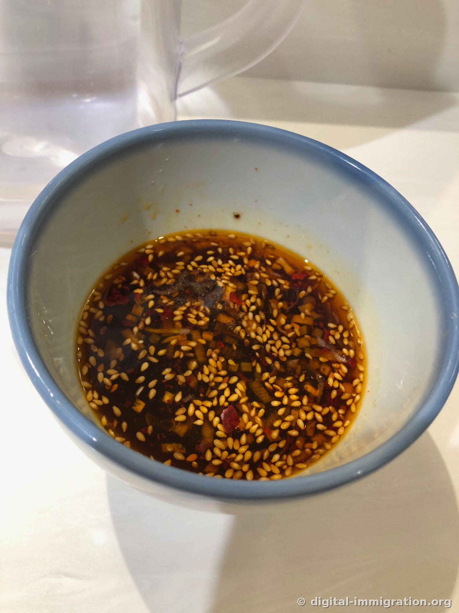 Empty blue-rimmed bowl with only sesame seeds, chili powder, and minced scallions left in red seasoning oil