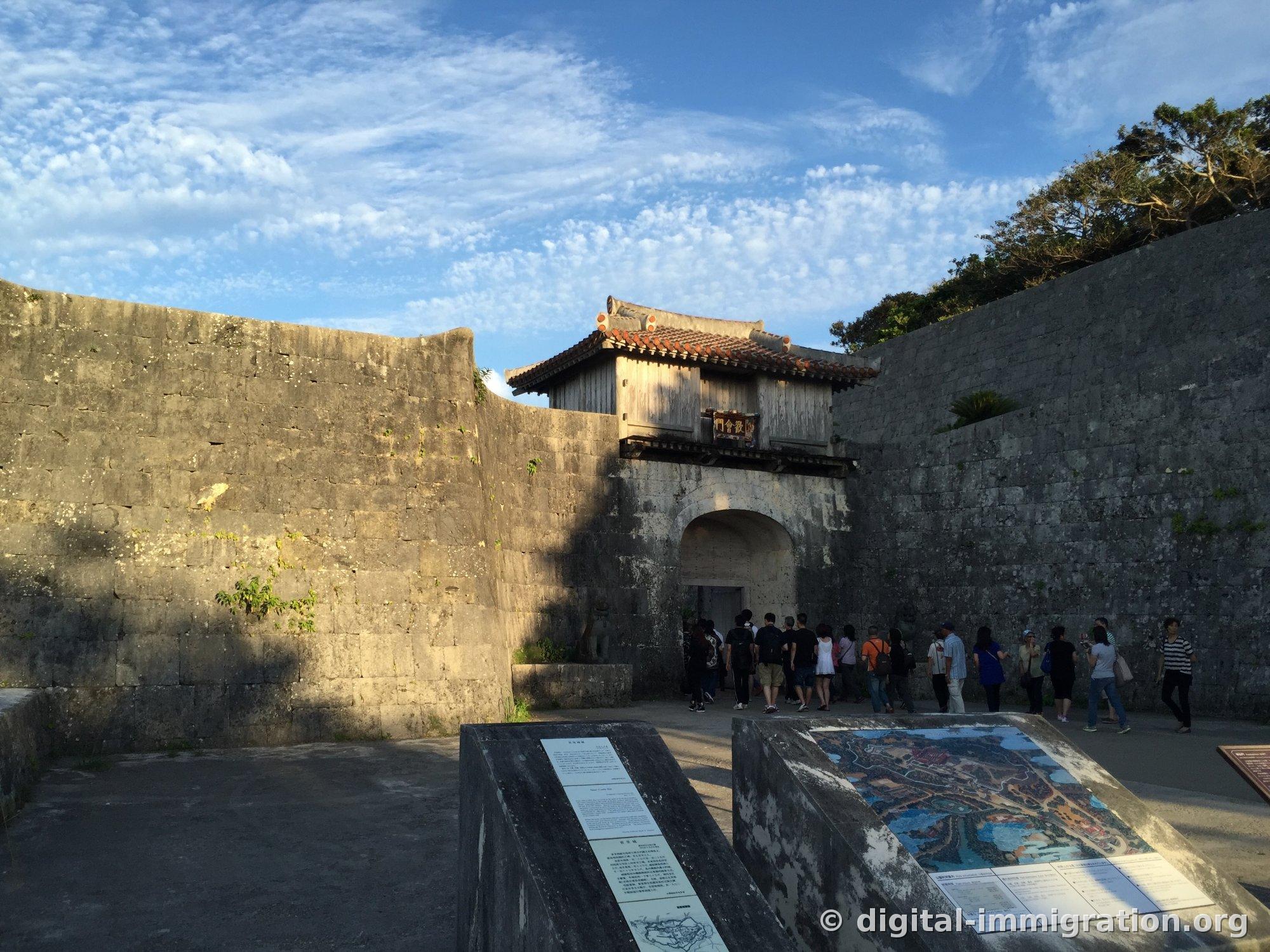 Kankaemon with its red-tiled gate tower atop curved limestone walls, tourists lined up in front of the arch
