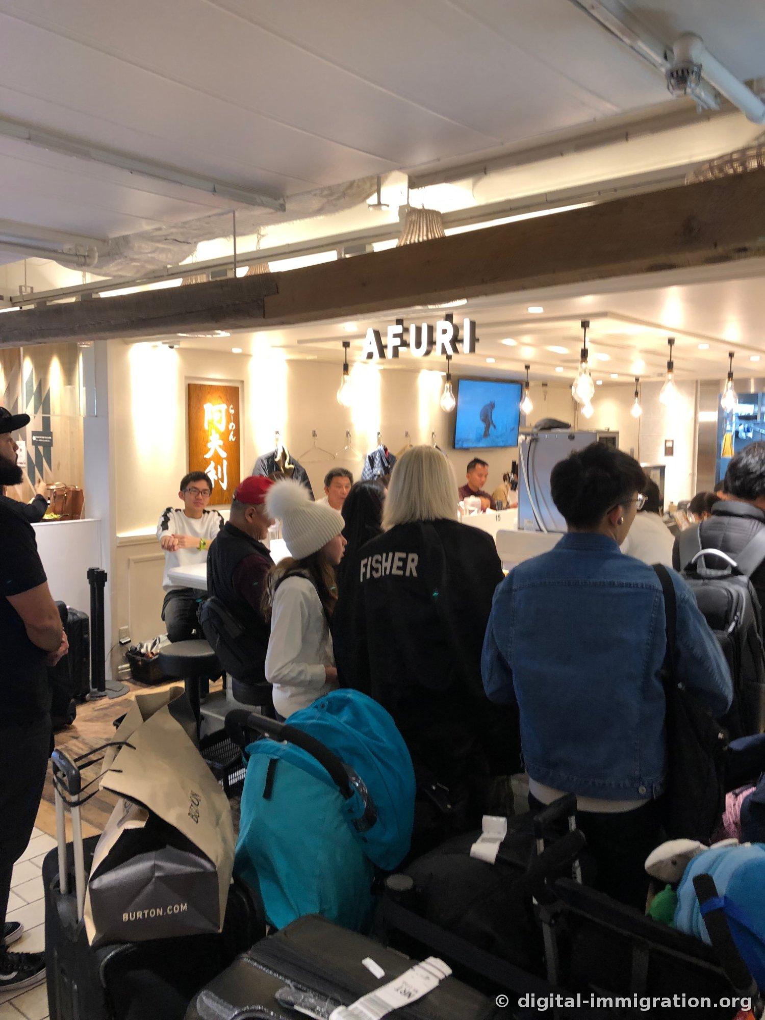 People with suitcases and backpacks waiting in a packed queue in front of the AFURI entrance, with a wooden 阿夫利 sign visible on the inner wall
