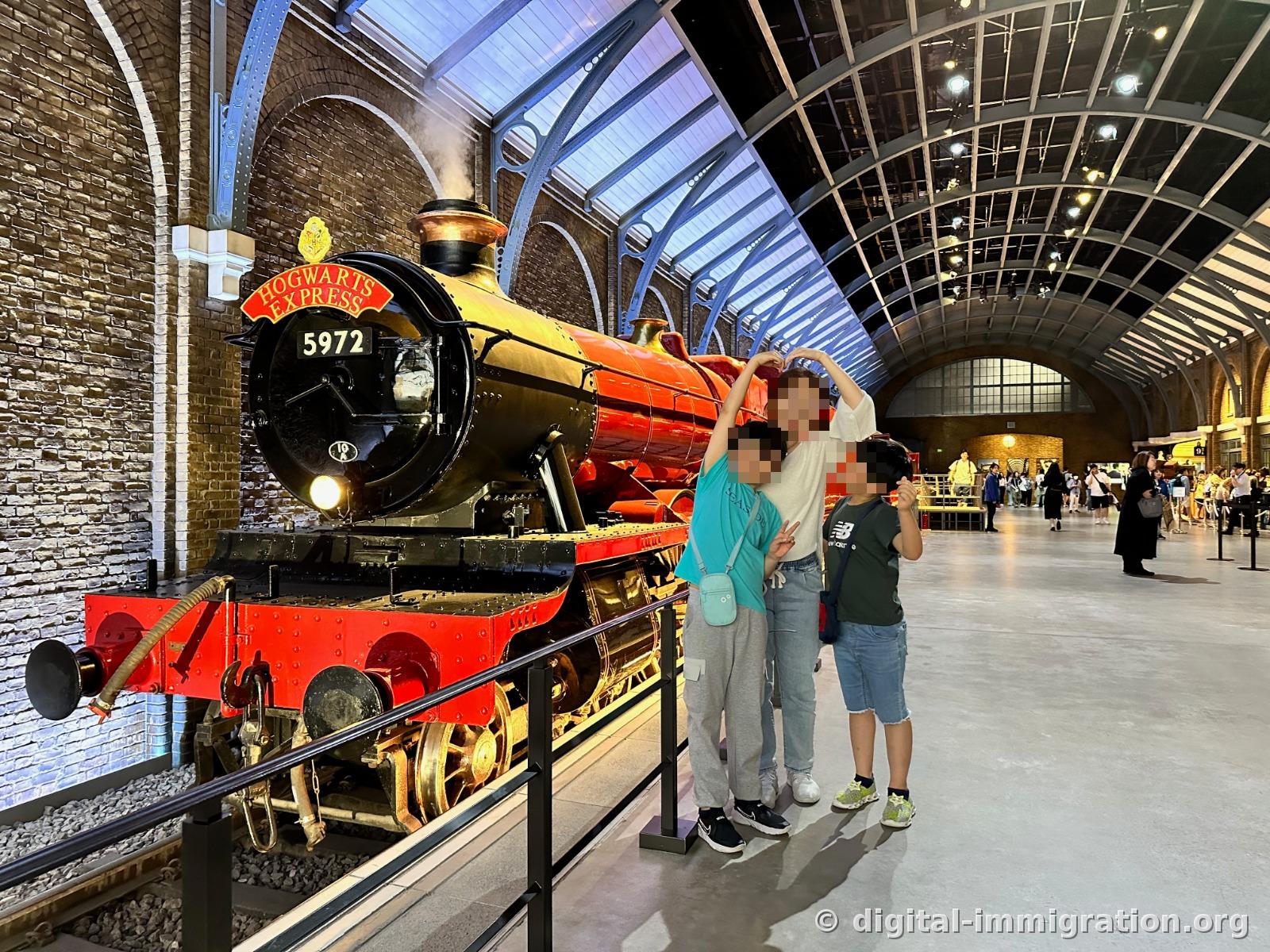 Three people posing in front of the Hogwarts Express locomotive under an arched glass roof
