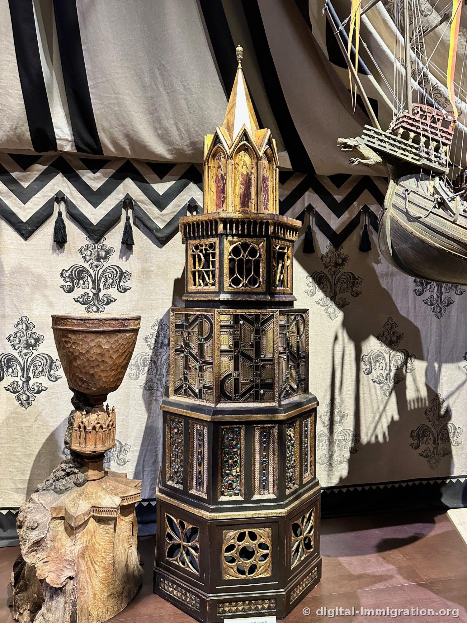 A wooden goblet and a gold-decorated octagonal box under a chevron tent, with a ship model suspended above