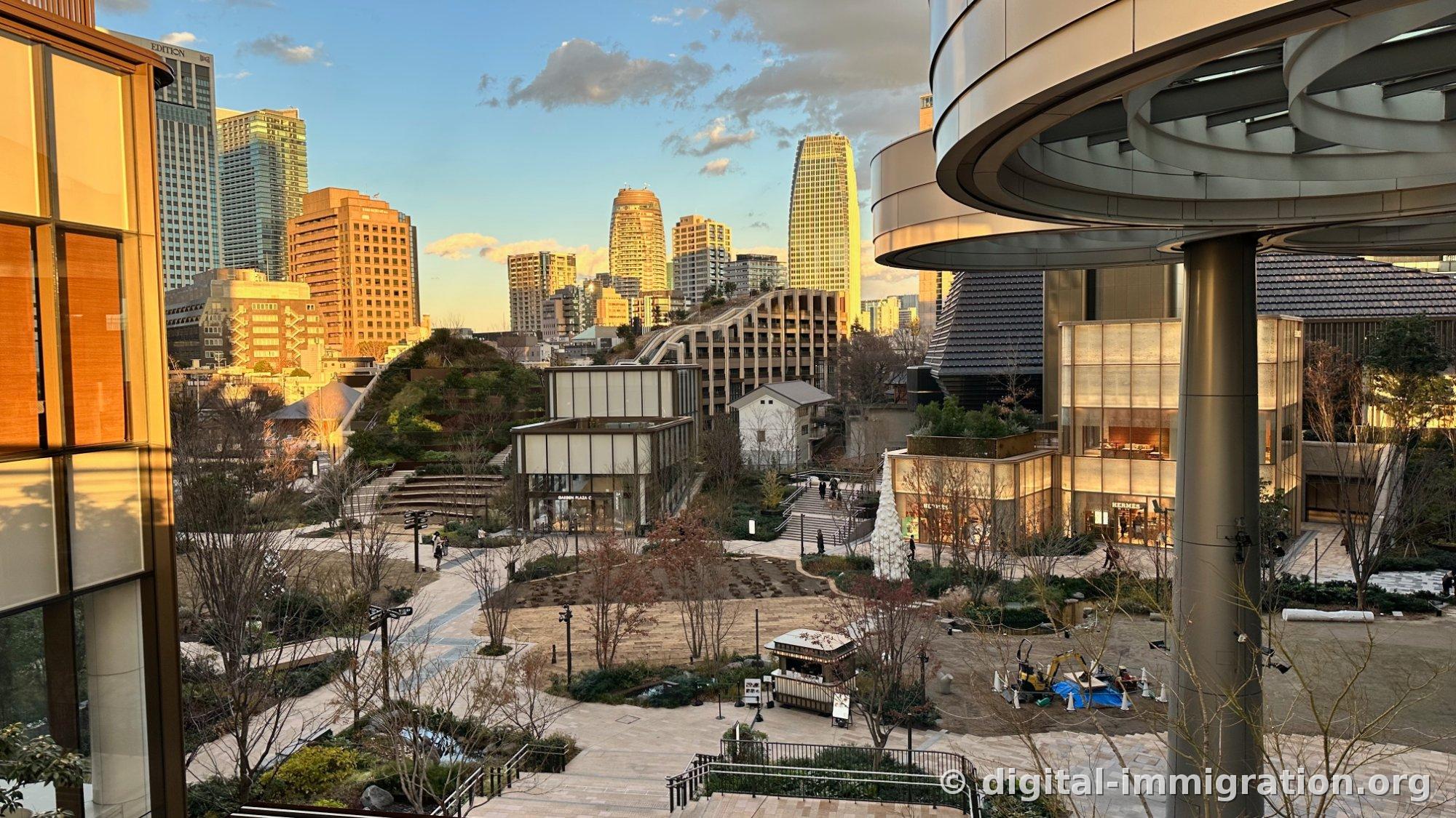 Overview of Azabudai Hills' terraced gardens at dusk, with EDITION hotel signage and Roppongi skyline on the left, metal canopy pillars on the right