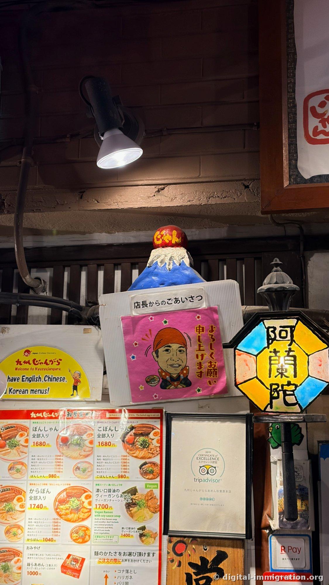 Miniature Mount Fuji, a caricature greeting sign from the owner, and stained glass reading Oranda displayed above the entrance, with ramen price list and TripAdvisor certificate below