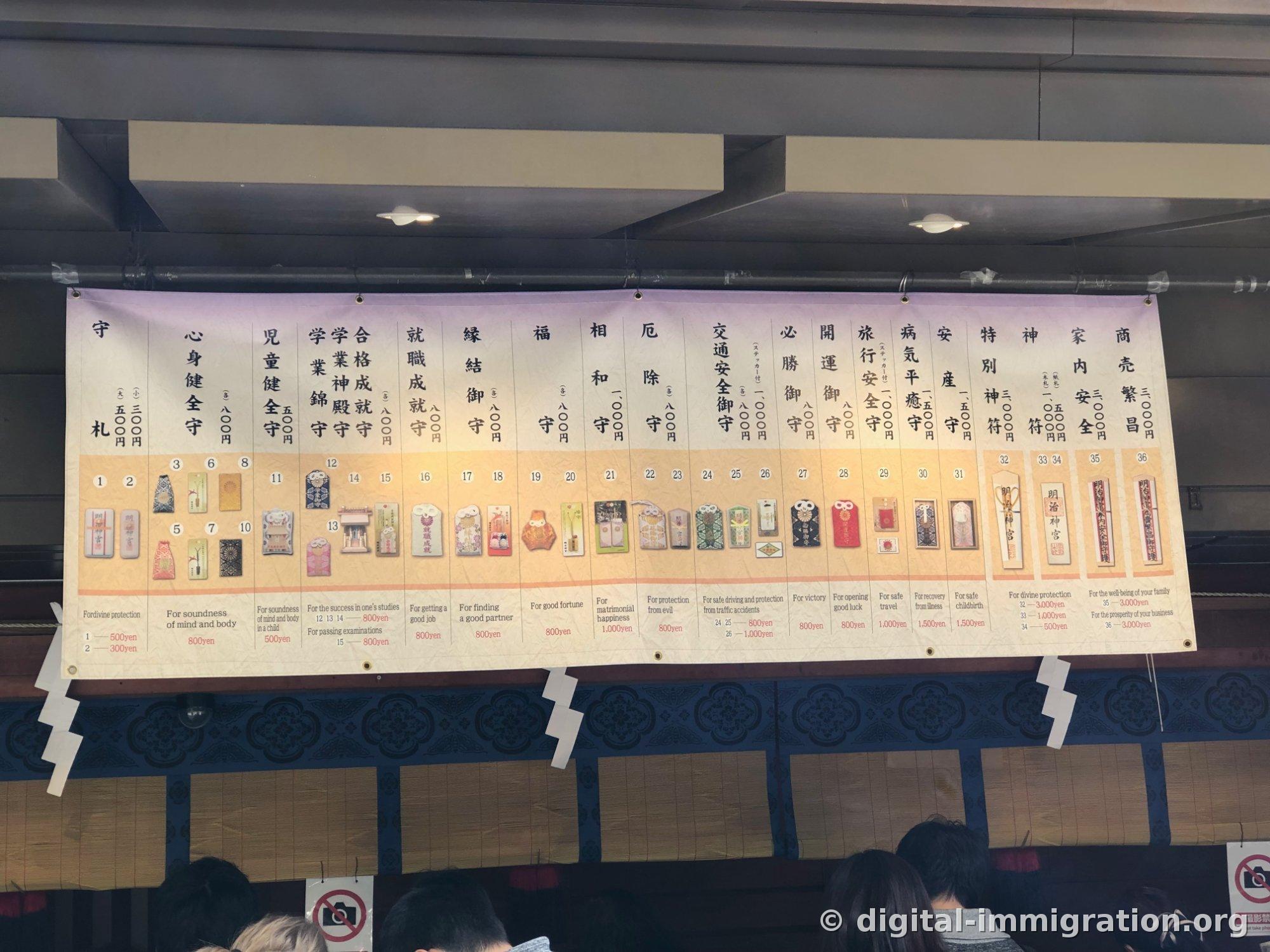 오마모리 종류와 가격이 일본어와 영어로 정리된 큰 현수막, 아래에 촬영 금지 표지