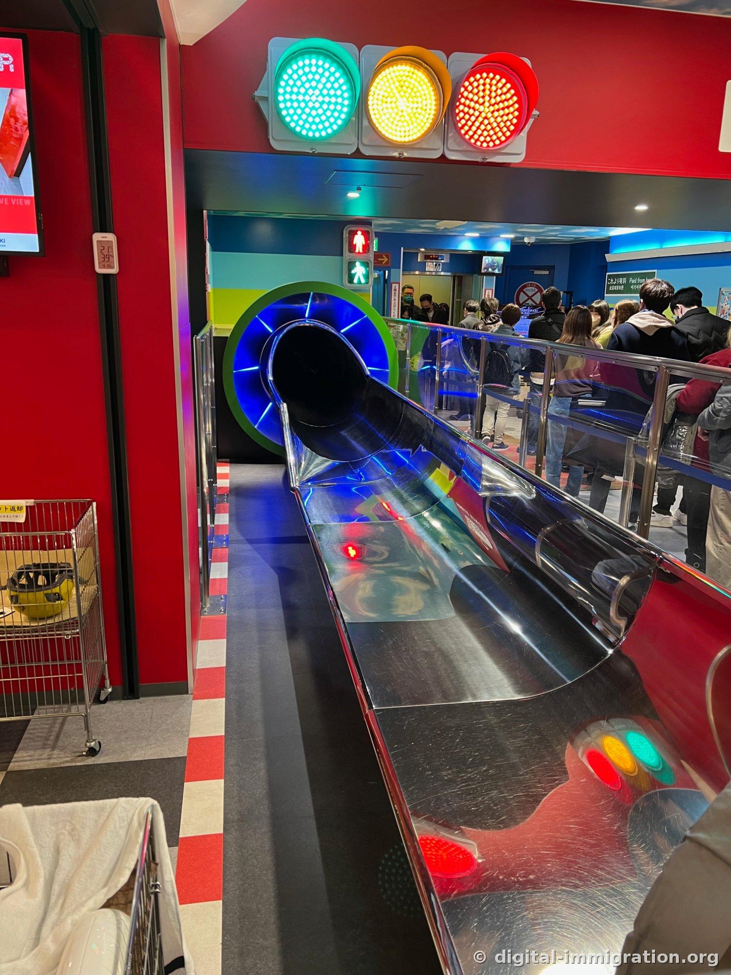 The Tower Slider starting point, with green, yellow, and red traffic lights lit above, a stainless steel slide leading to a blue circular tunnel entrance