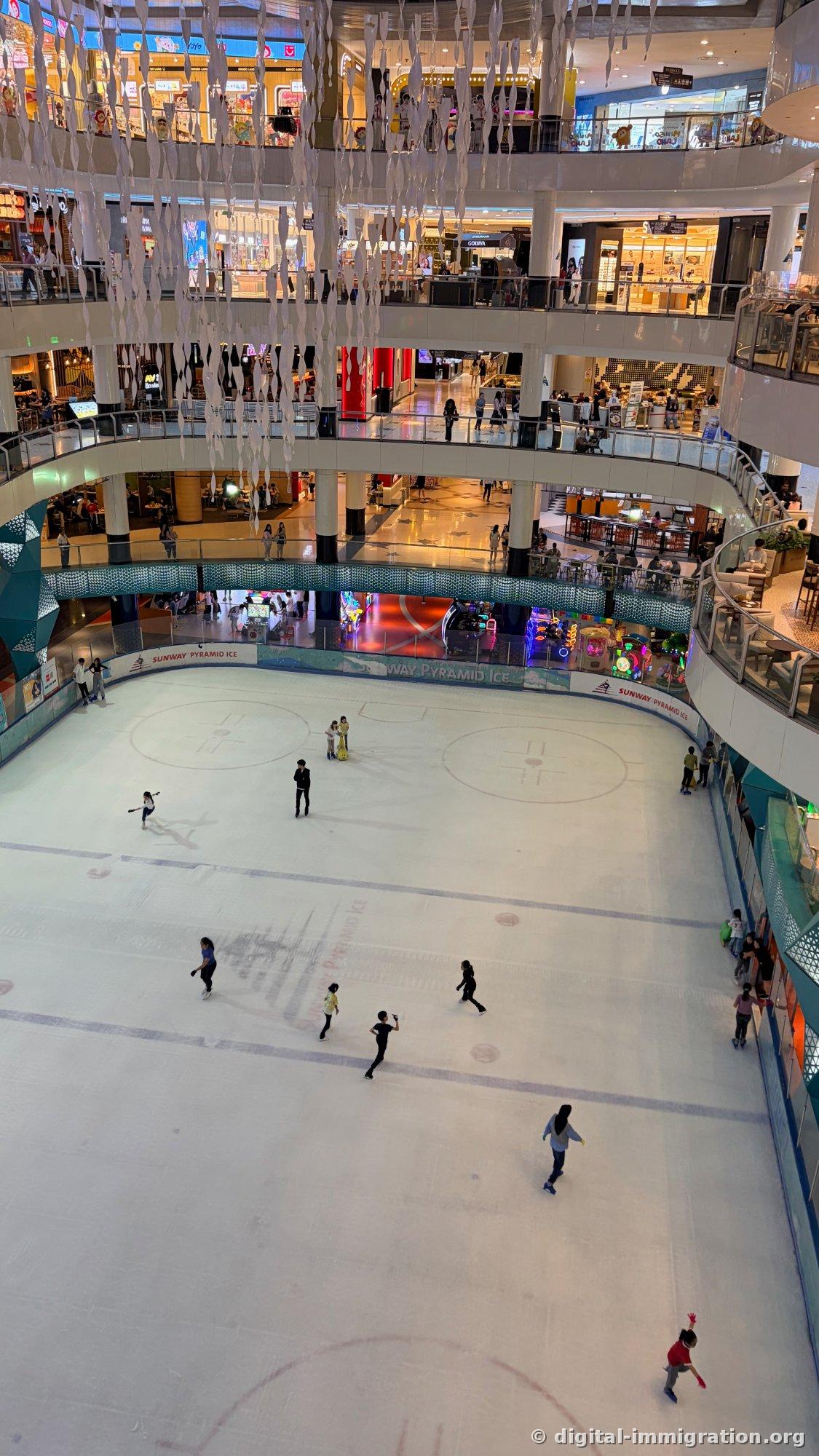 从商场多层楼下方看到的 Sunway Pyramid Ice 室内冰场和在其上滑冰的人们