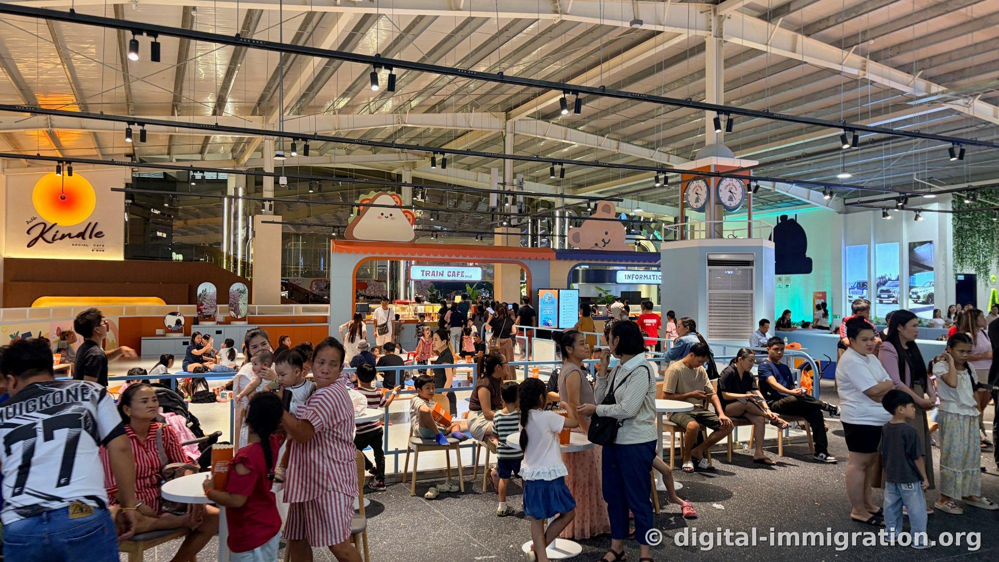 TRAIN CAFE signage and pastel-colored kids' zone with families sitting, clock tower-style column