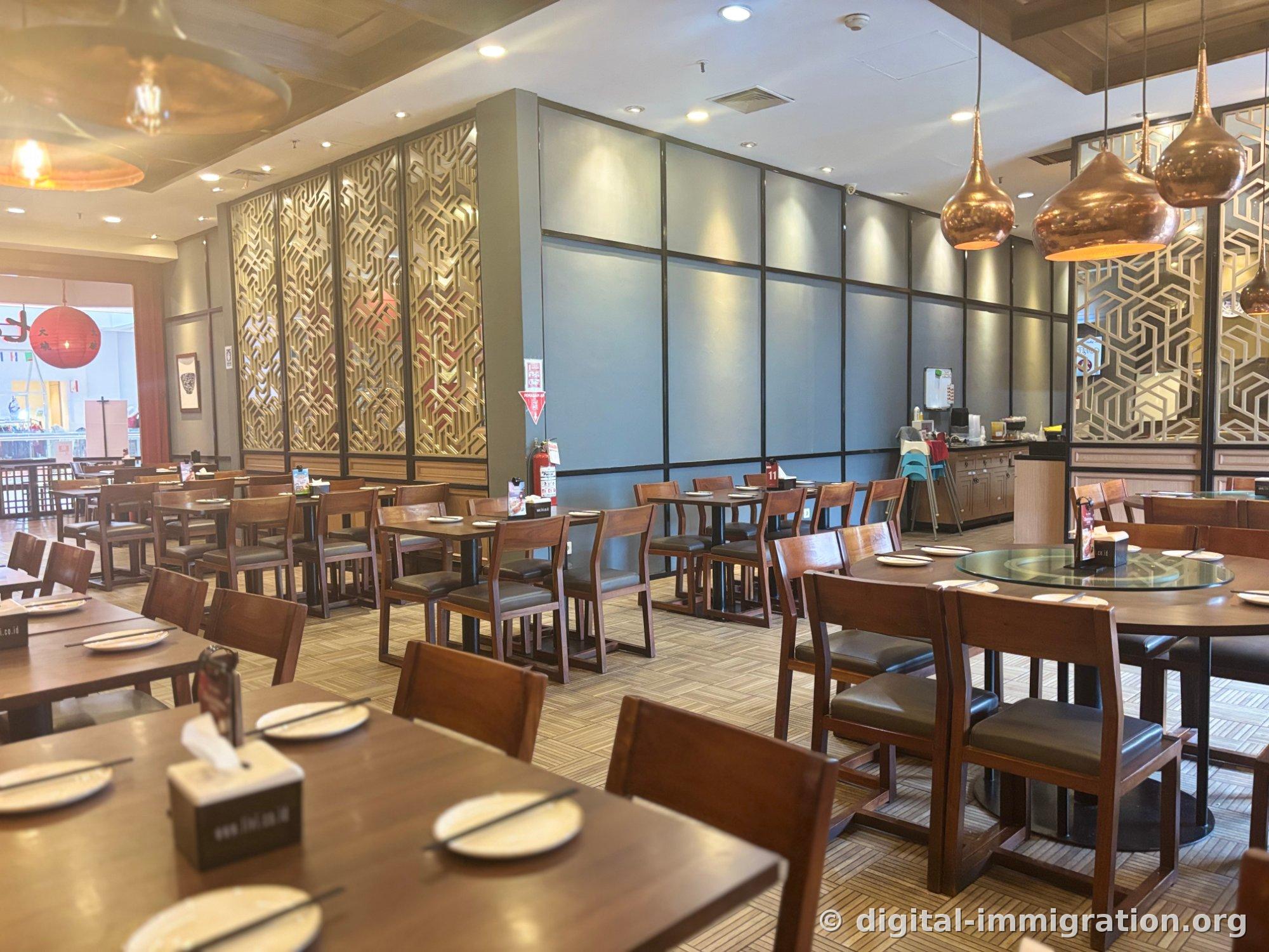 Ta Wan's interior with wooden tables and chairs in rows, gold lattice partitions and copper-colored pendant lighting, with a round table featuring a lazy susan on the right side