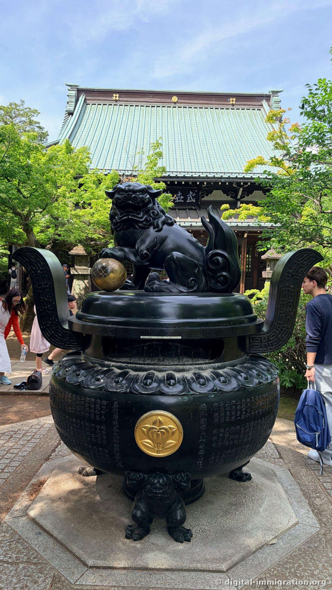 A large bronze incense burner with lion statues and a gold sphere on top, with a verdigris-roofed Buddhist hall behind it