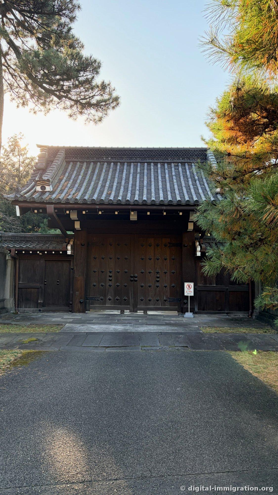 Une vieille porte en bois noir fermée sous la lumière contre-jour, avec un toit de tuiles, et un panneau d'interdiction d'accès à droite