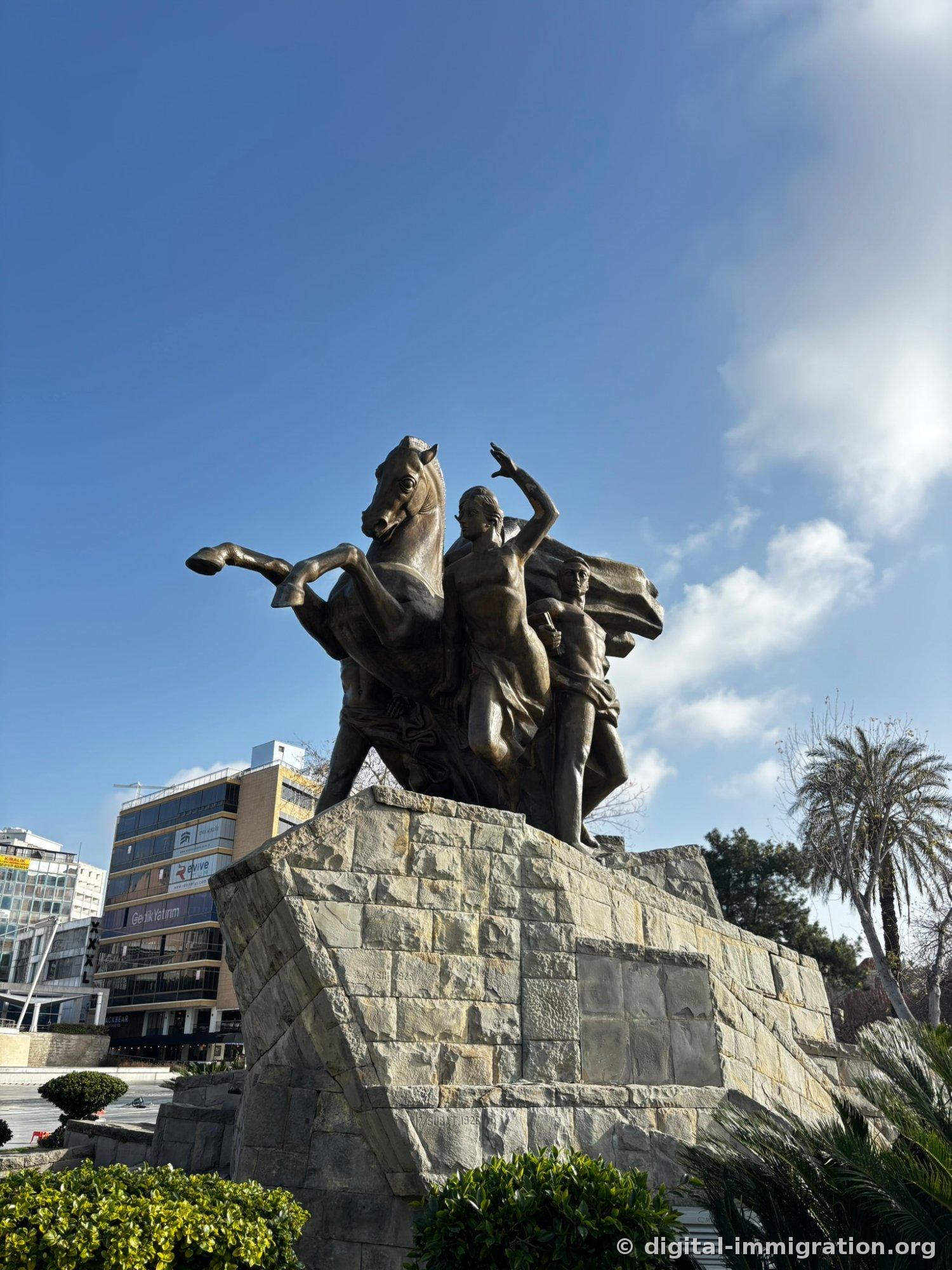 The bronze equestrian statue of Cumhuriyet Square. A horse with raised front legs and figures with outstretched arms stand on a stone base, with modern office buildings and palm trees visible behind.