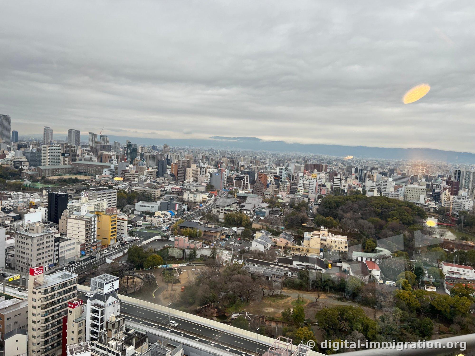 Osaka cityscape spread out beyond the observation deck's glass, with low clouds, and the Tennoji Zoo and expressway visible below