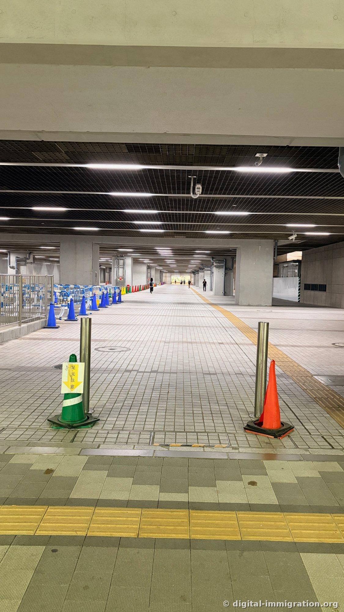 Large passage piéton souterrain avec des rangées de néons, des barrières bleues et des cônes de chantier d'un côté