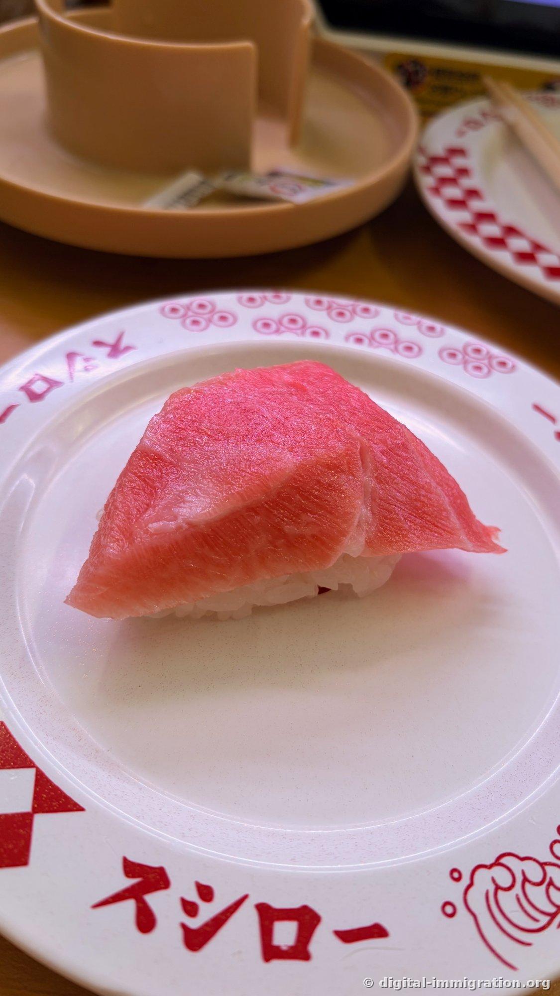 Un morceau de sushi toro avec du gras densément marbré posé sur une assiette blanche marquée du logo Sushiro