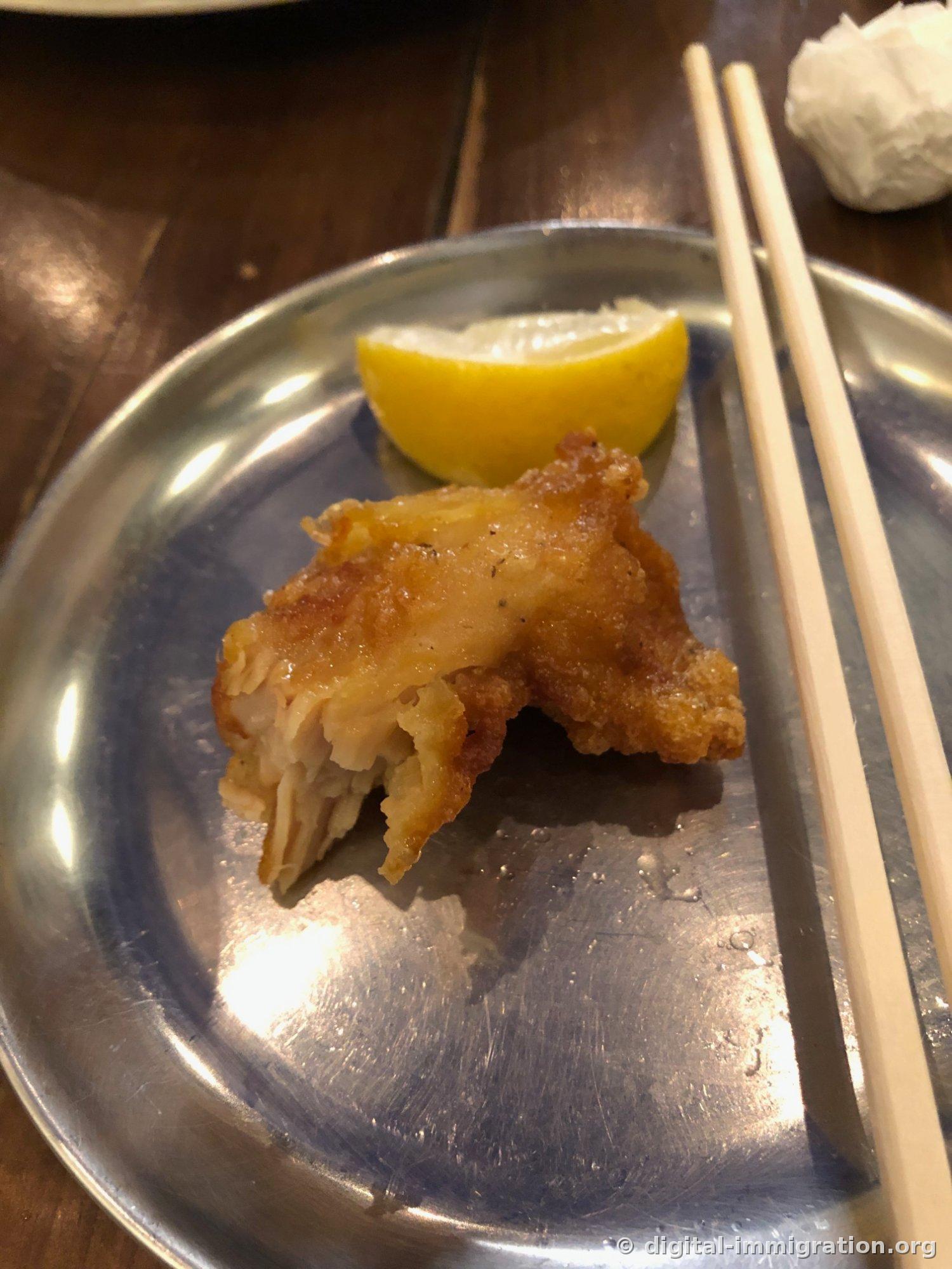 银色盘子上最后一块炸食，一片柠檬，旁边放着竹筷
