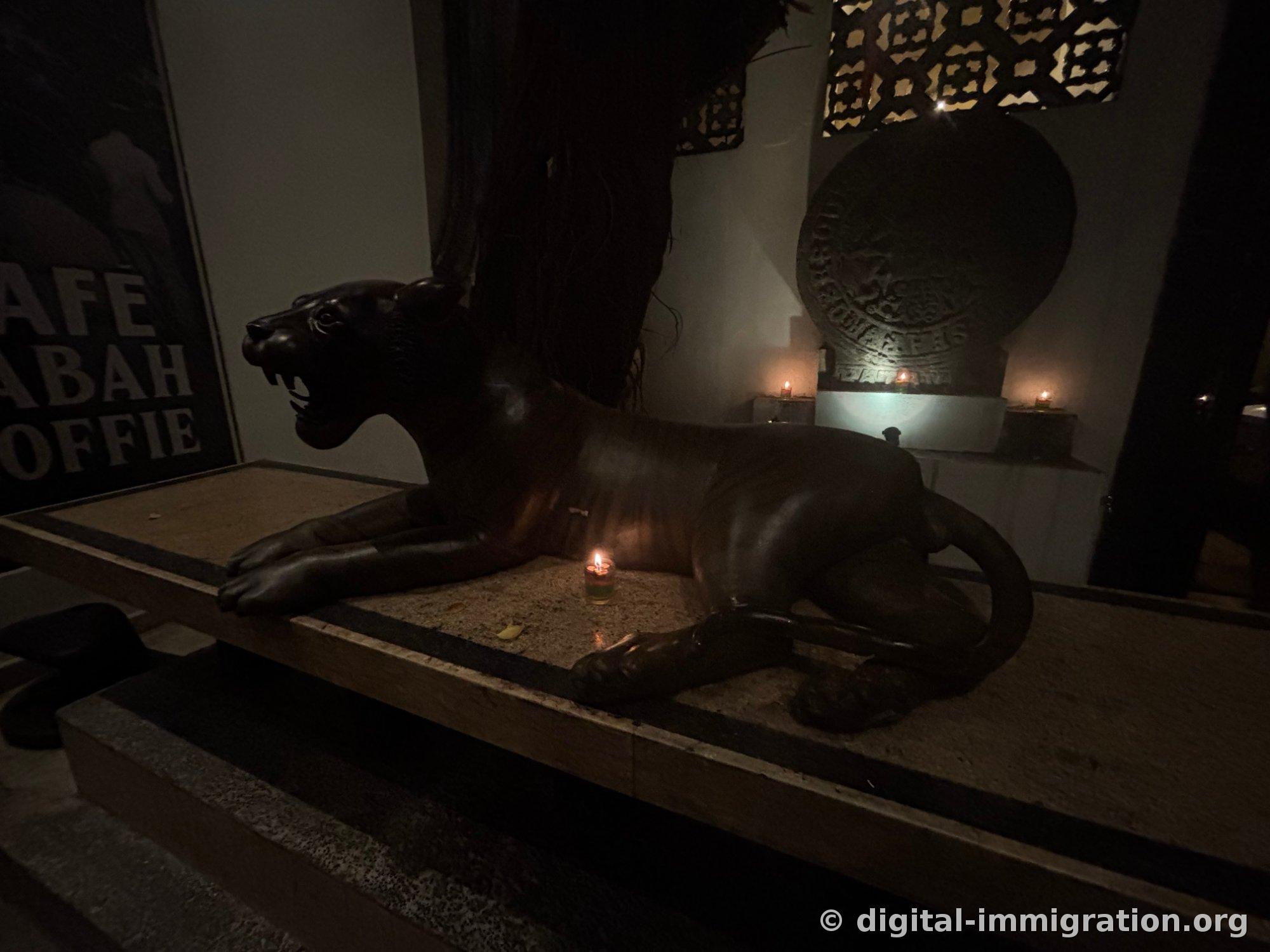 Black leopard sculpture stretched out on a low platform inside dark room with single lit candle in front
