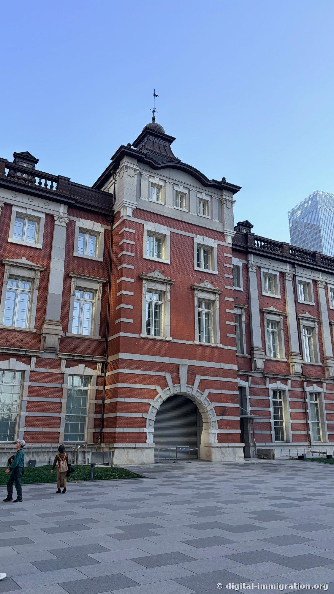 Le côté nord du bâtiment historique de la Gare de Tokyo Marunouchi avec les briques rouges et les ornements en pierre blanche, l'entrée en arche et deux personnes qui la traversent
