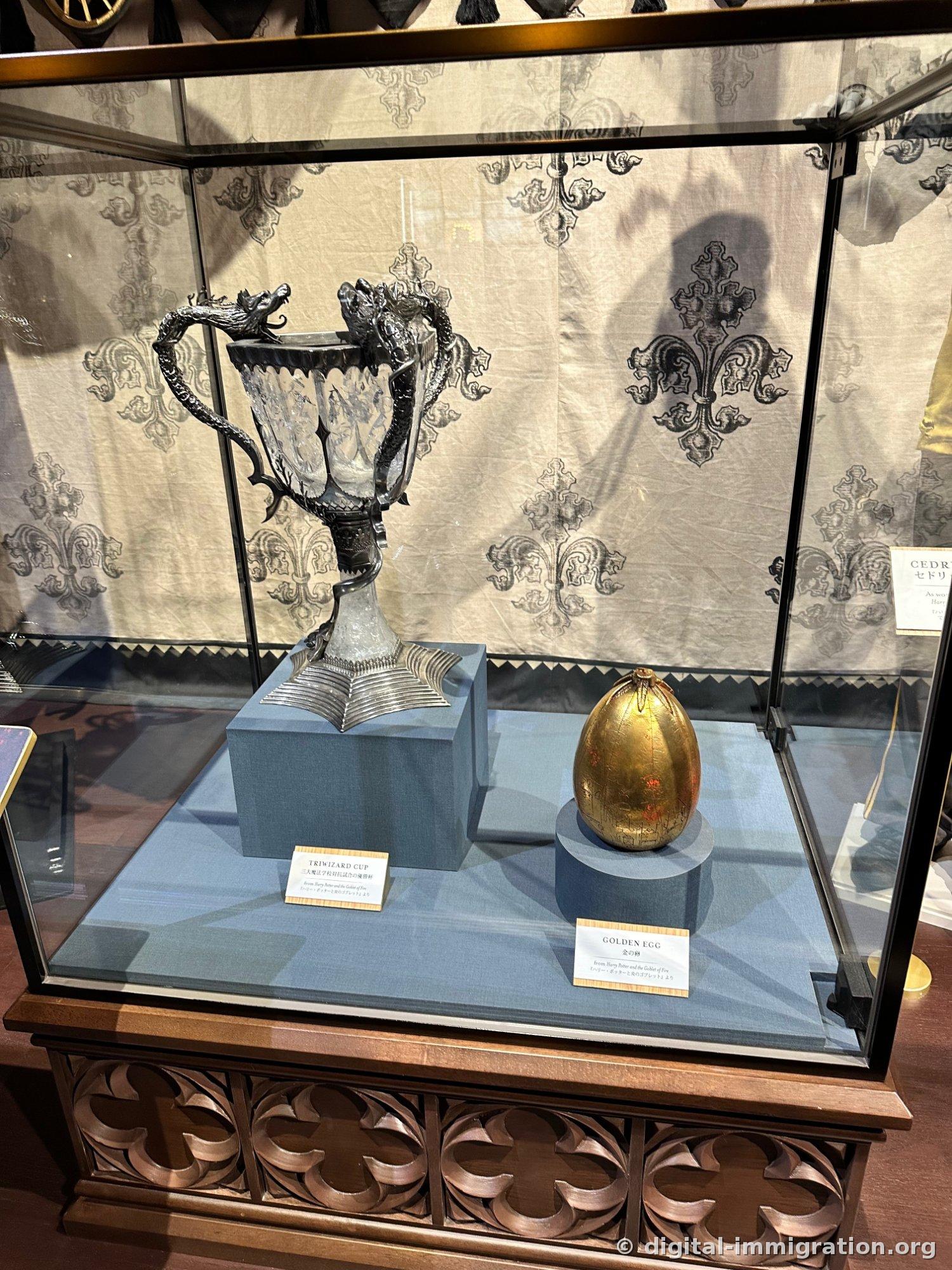 A silver cup with dragon handles and a golden sphere on a blue pedestal in a glass case
