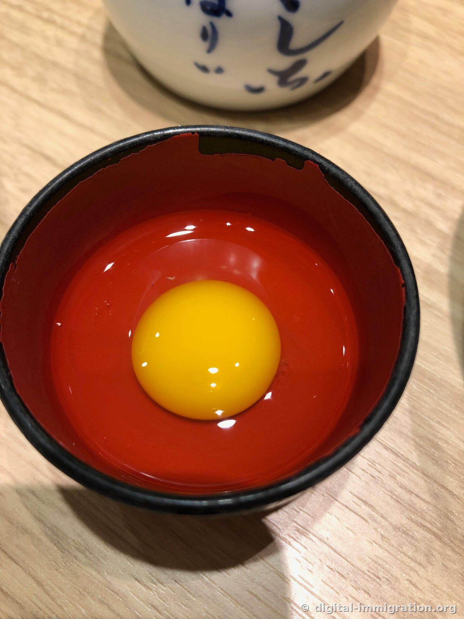 A close-up of a round raw egg yolk in a red lacquered dish