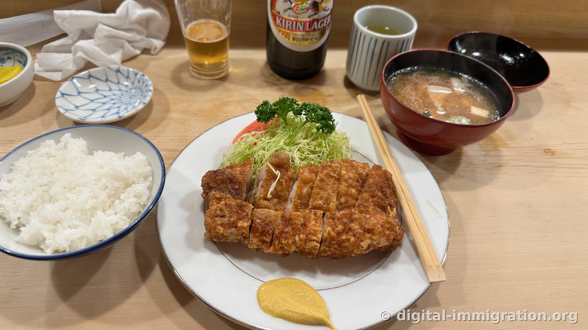 A roast cutlet set meal on a white plate with shredded cabbage and parsley, a dollop of mustard, a bowl of white rice, miso soup in a red lacquer bowl, and pickled daikon