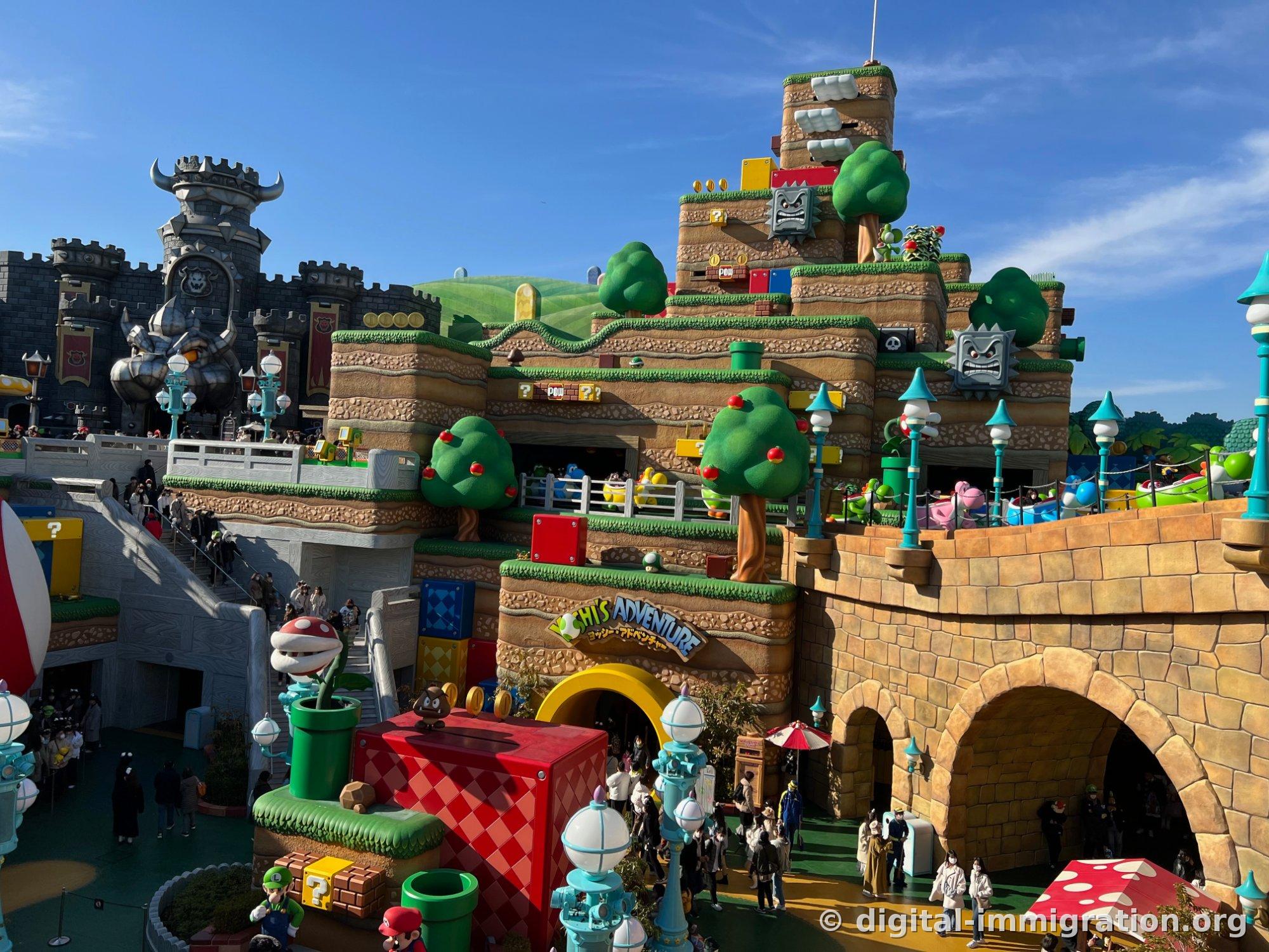 Super Nintendo World hills in afternoon sunlight. The Yoshi Adventure sign is visible, along with a Piranha Plant emerging from a green pipe and a red box with a Goomba on top