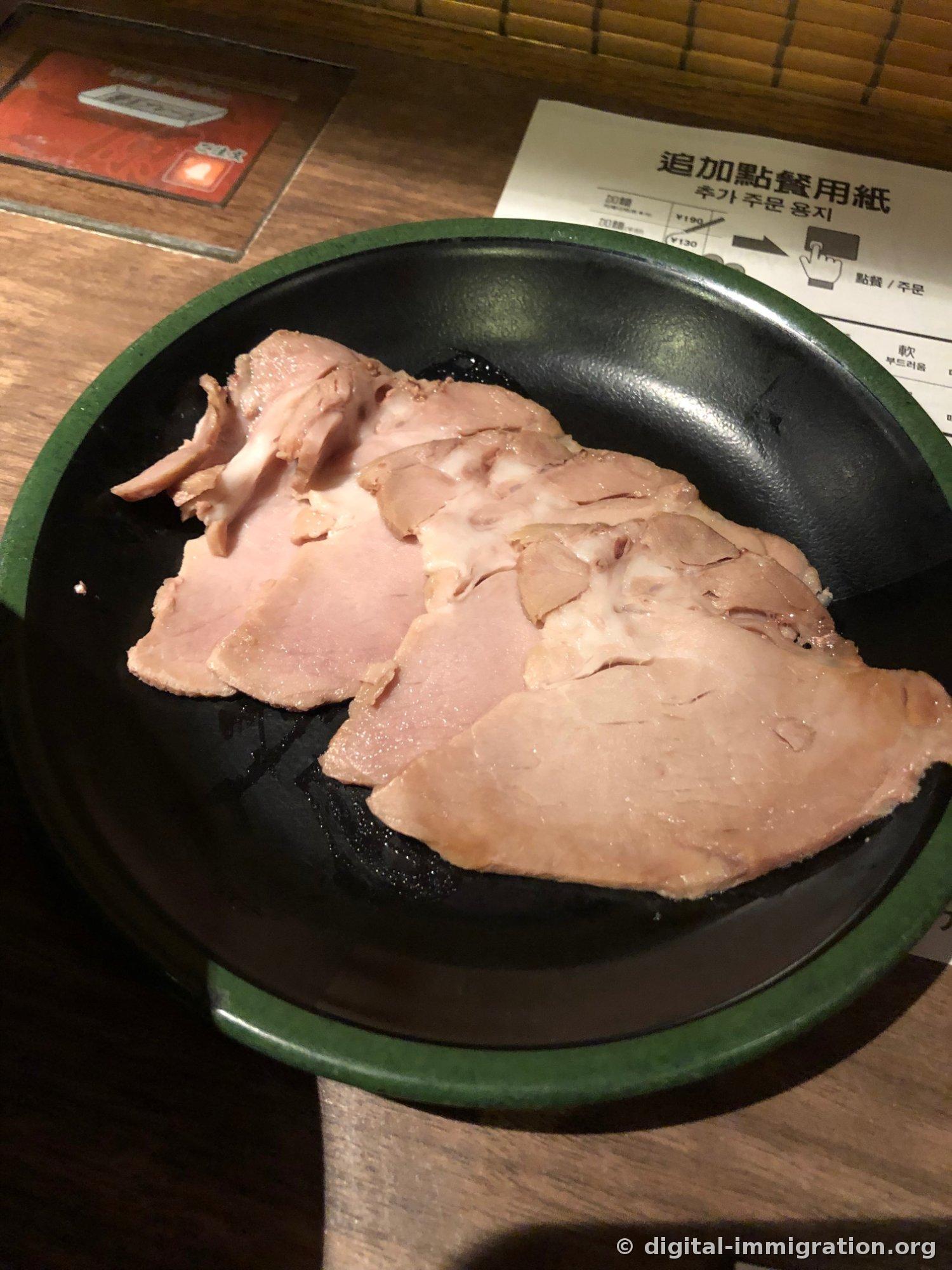 Quatre tranches de char siu finement émincées superposées sur une assiette noire