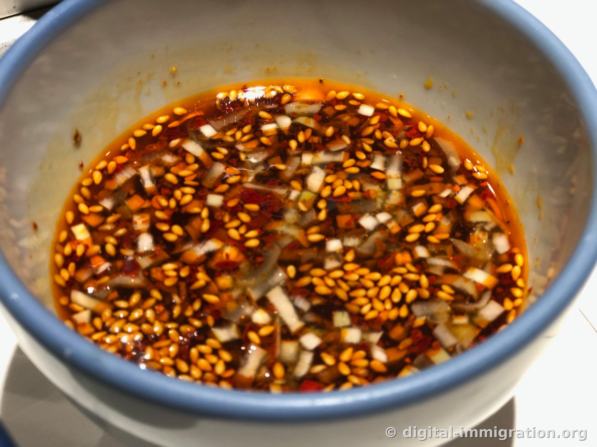 Close-up of bowl bottom with sesame seeds, white scallion pieces, and chili powder floating in red chili oil