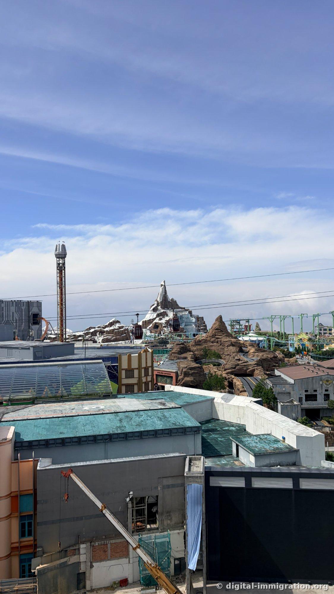 SkyWorlds snow peak set and drop tower under clear sky with cable car cables, teal-roofed building in front and construction crane