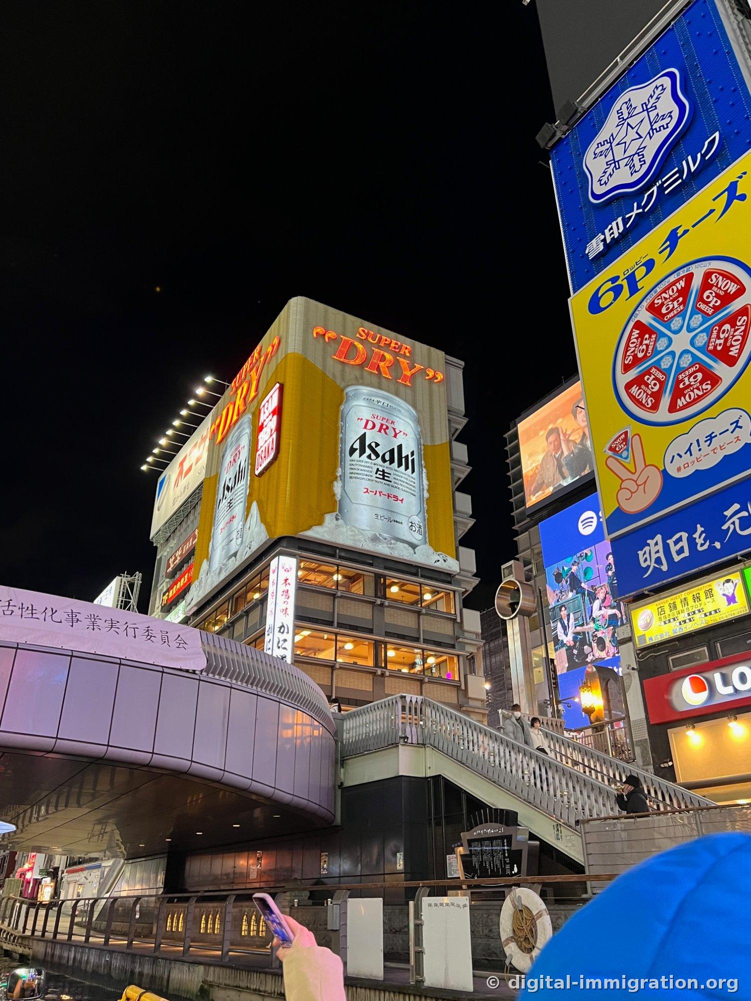 Sous un ciel nocturne nuageux, un immeuble éclairé multi-étages et bâtiments bas avec enseigne cinéma Tatsumi