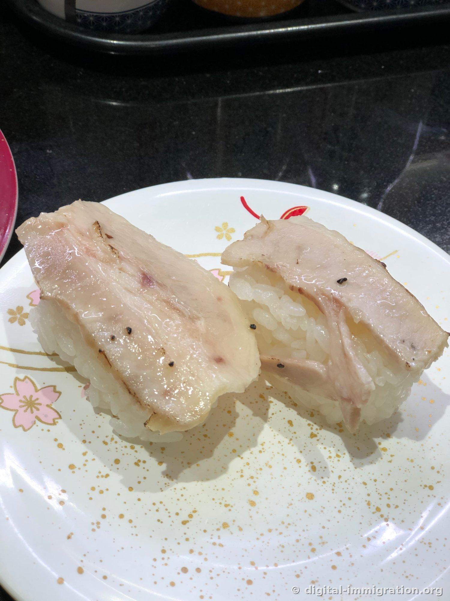 樱花纹白色盘子里装着的炙烧白鱼寿司两贯，表面轻轻炙过，点缀着黑胡椒粒