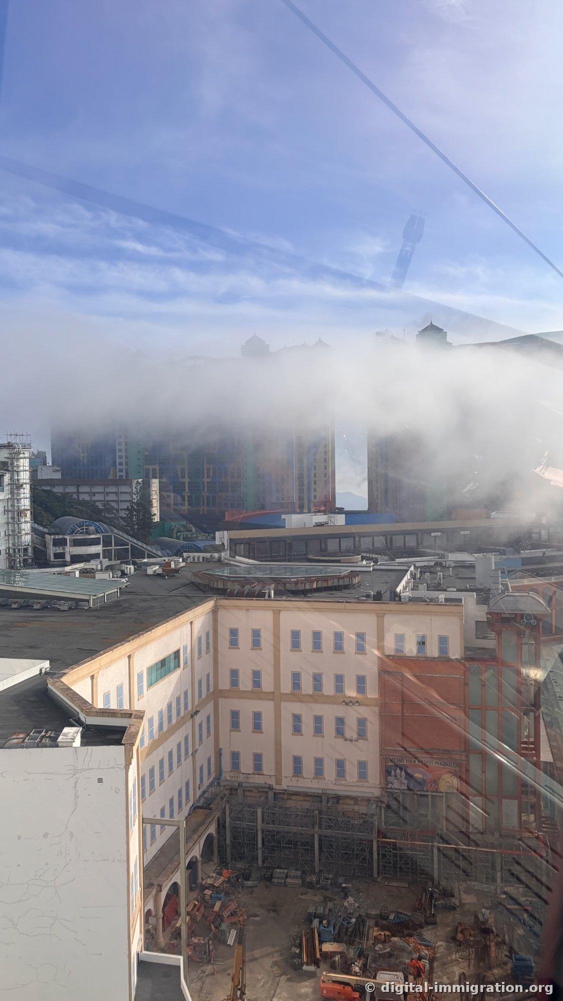 Buildings at Genting peak partially obscured by flowing clouds beyond window glass, construction site visible