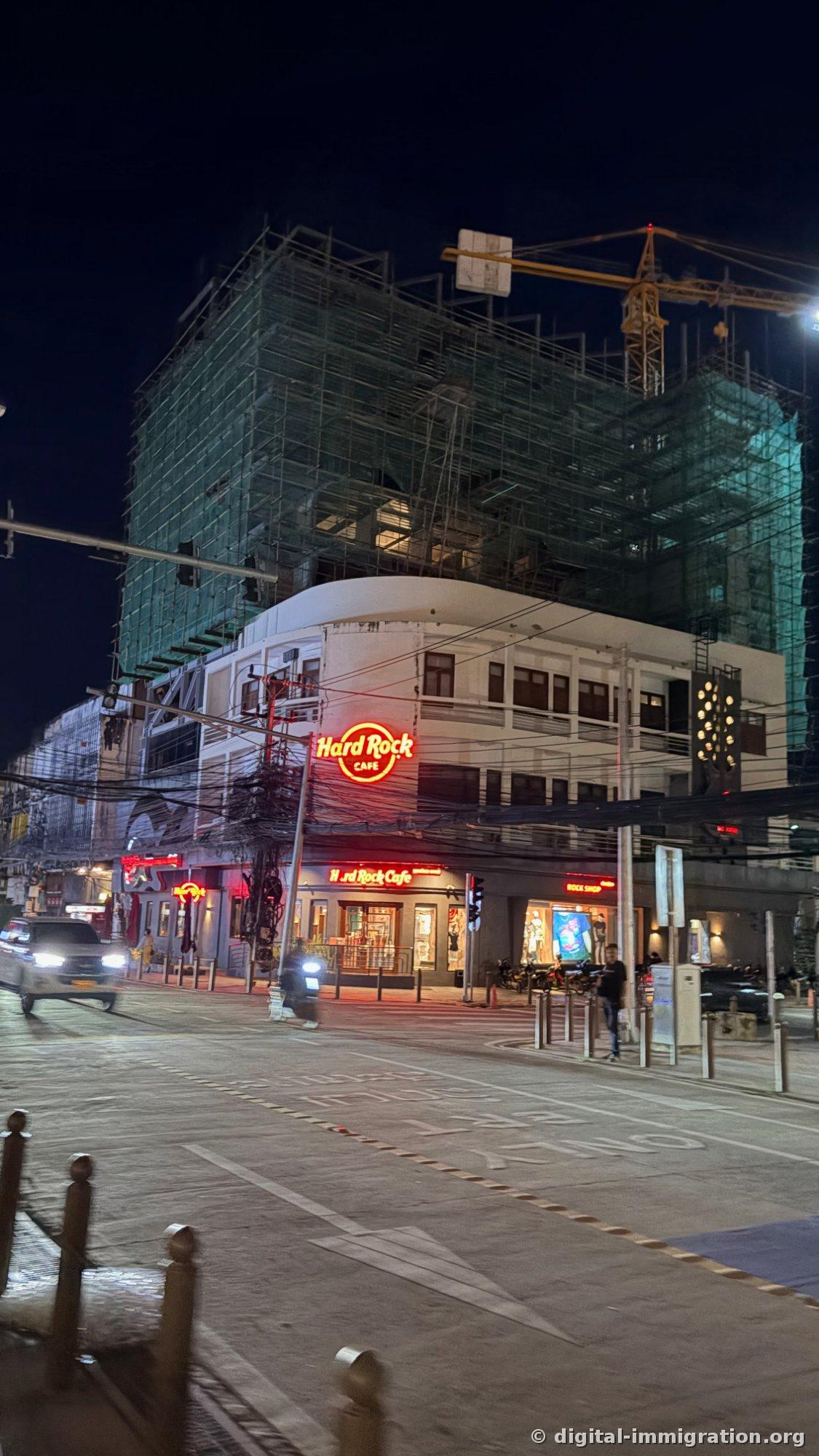 밤에 사거리 건너편에서 본 Hard Rock Cafe 건물, 뒤쪽에 녹색 안전망을 씌운 공사 중 고층 건물과 노란 타워크레인