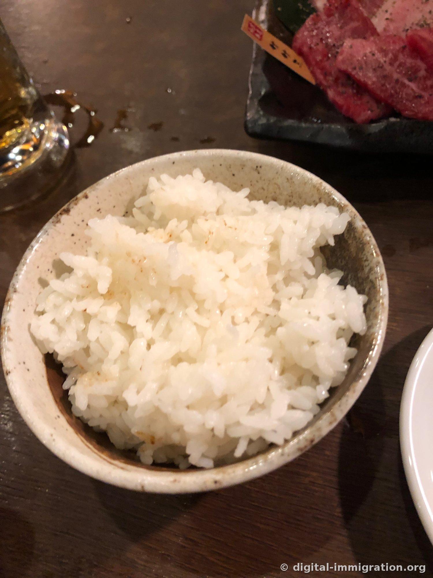 Riz blanc dans un bol de céramique rustique avec une assiette de viande crue à côté et un verre de bière