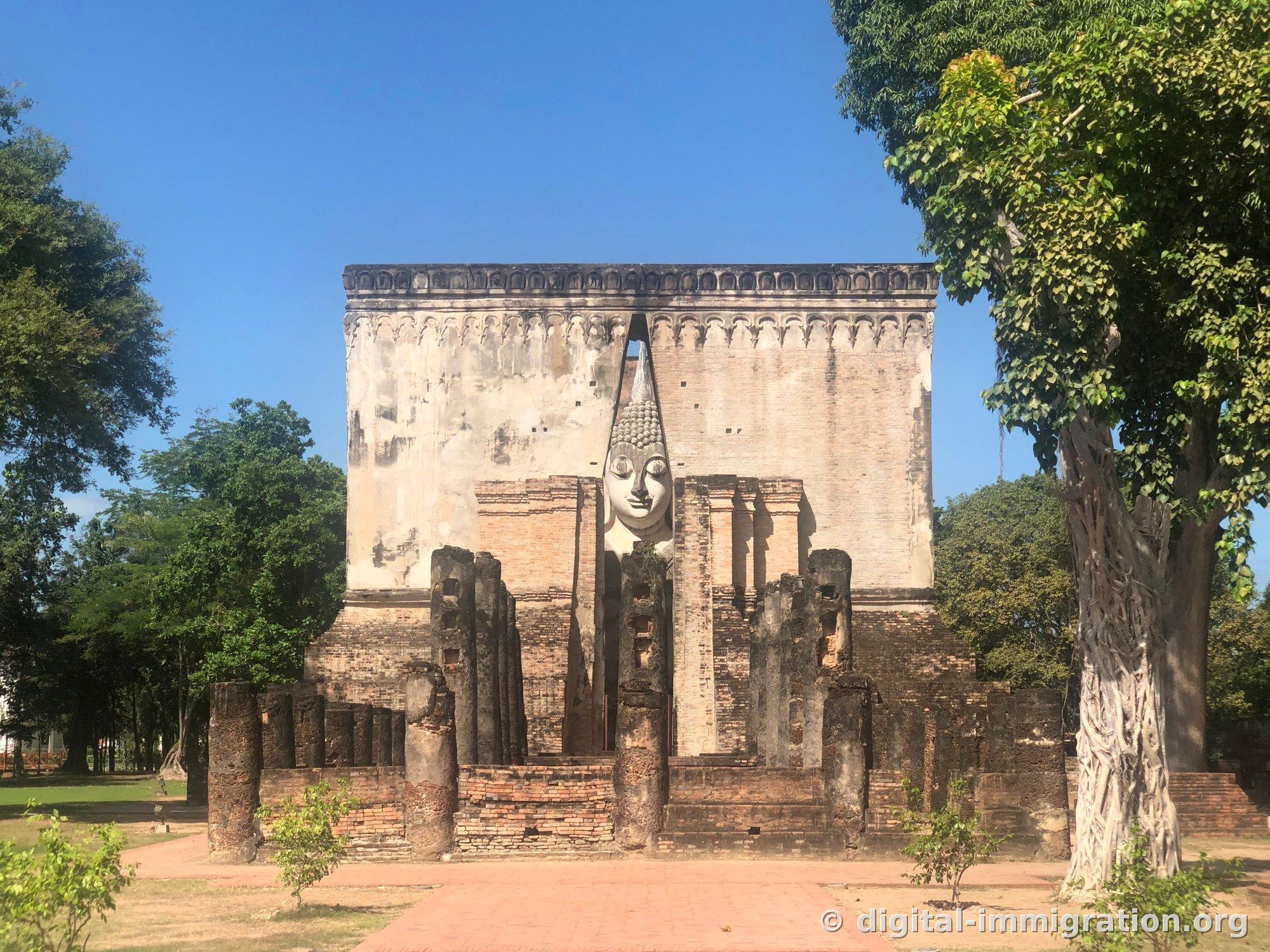 Wat Si Chum, a rectangular brick building with no windows, with a narrow vertical gap in the center of the front through which the face of a white seated Buddha inside can be seen