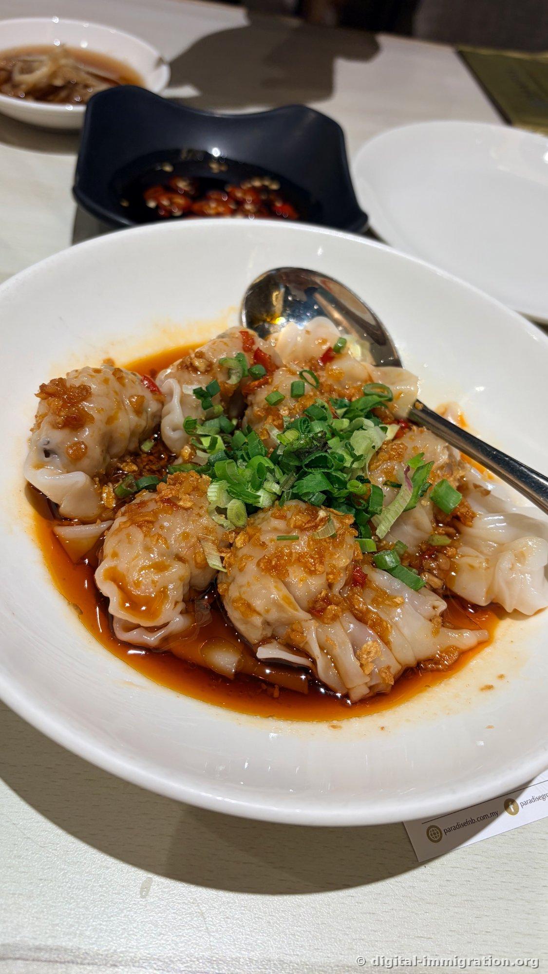 Wonton in red chili oil on white plate with fried garlic and scallions sprinkled on top