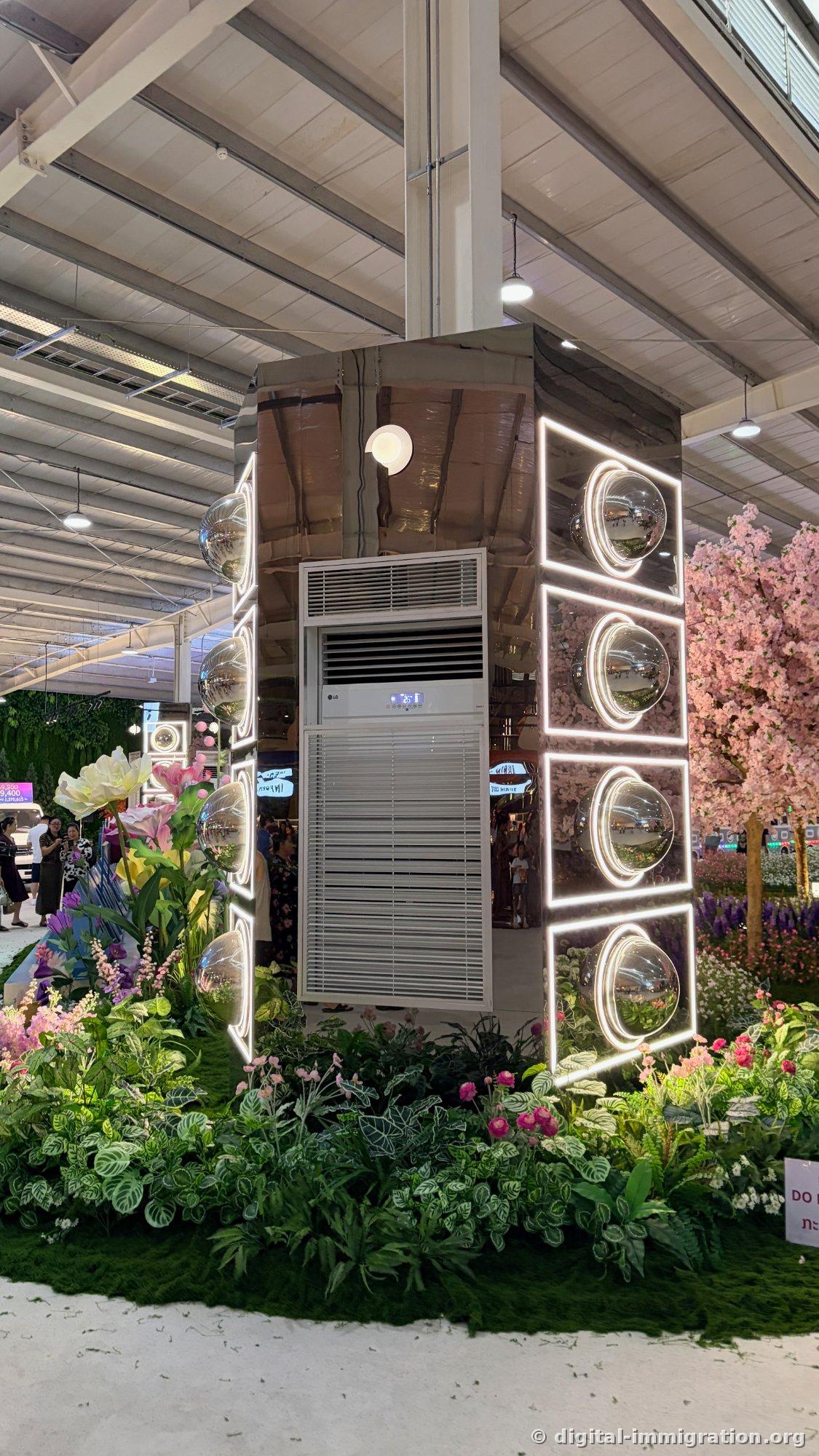 LG pedestal air conditioner in center of flower garden decorated with mirror panels, lighting frame, and silver spheres