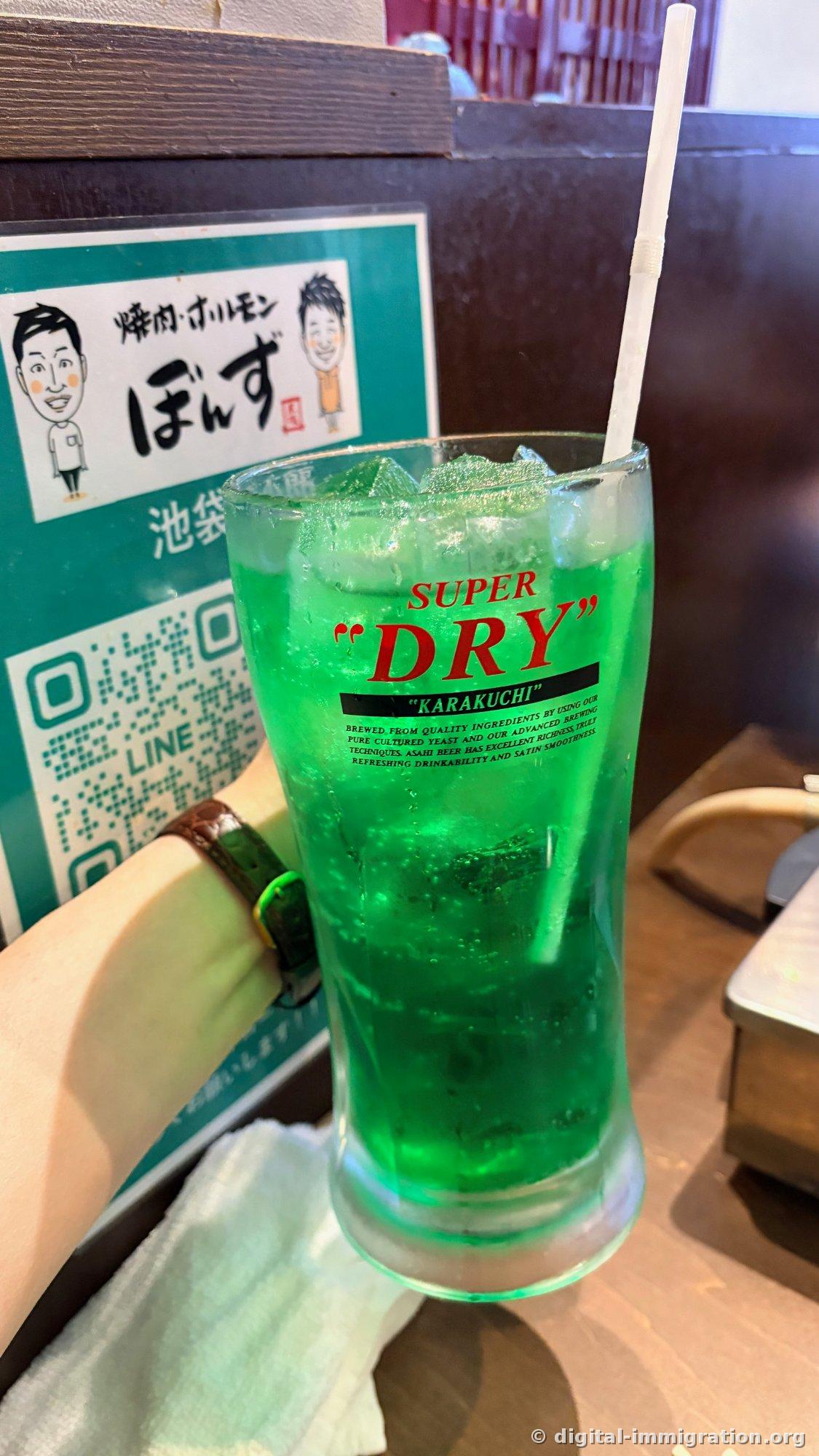 Neon-green melon soda in a glass stamped with the Asahi Super Dry logo; behind it a green sign with the restaurant logo and LINE QR code