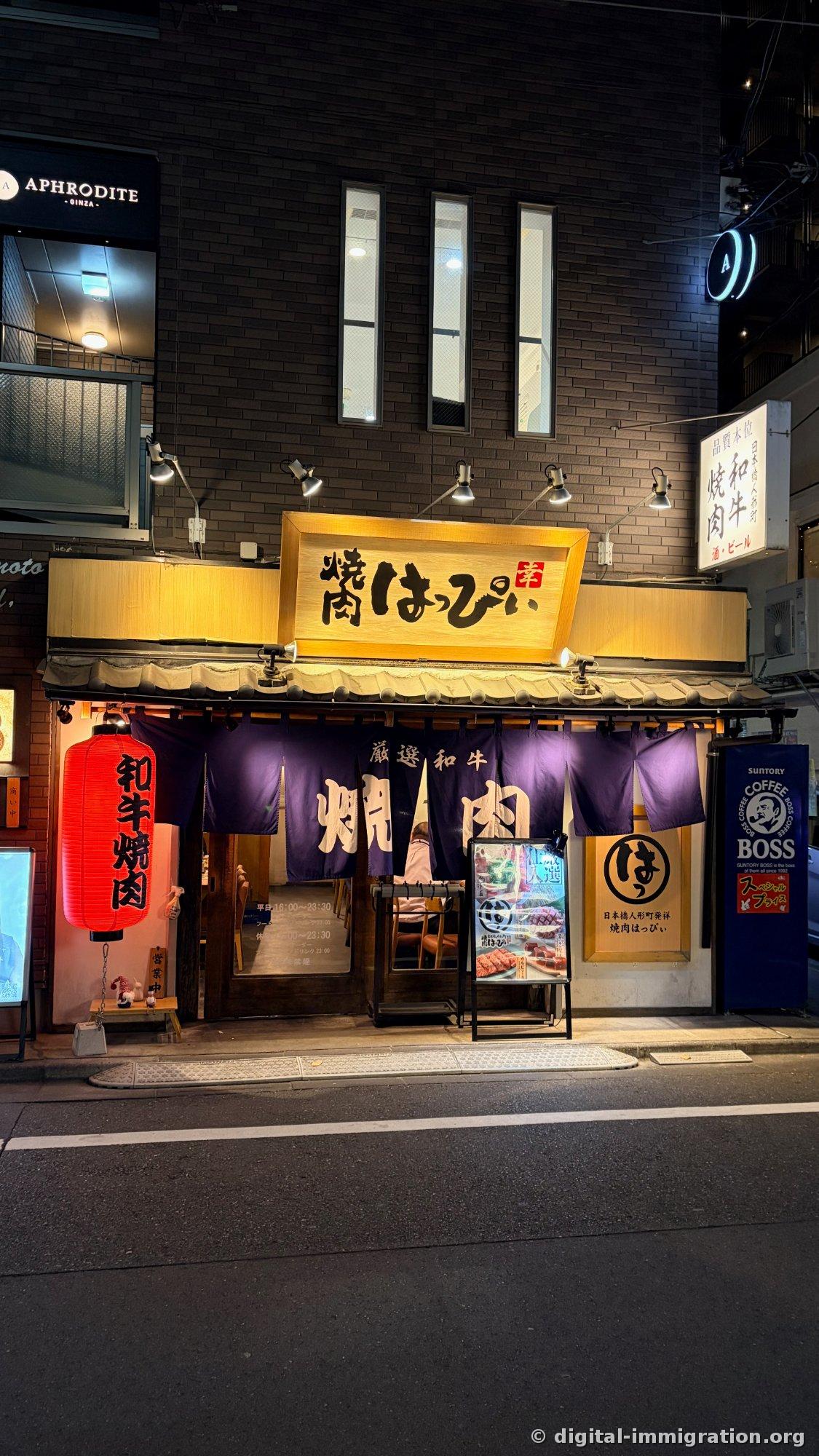 Night photo of Yakkiniku Happi's exterior. Yellow wooden sign reads '焼肉はっぴぃ', a red lantern on the left says '和牛焼肉', and a purple noren curtain displays '厳選和牛 焼肉'