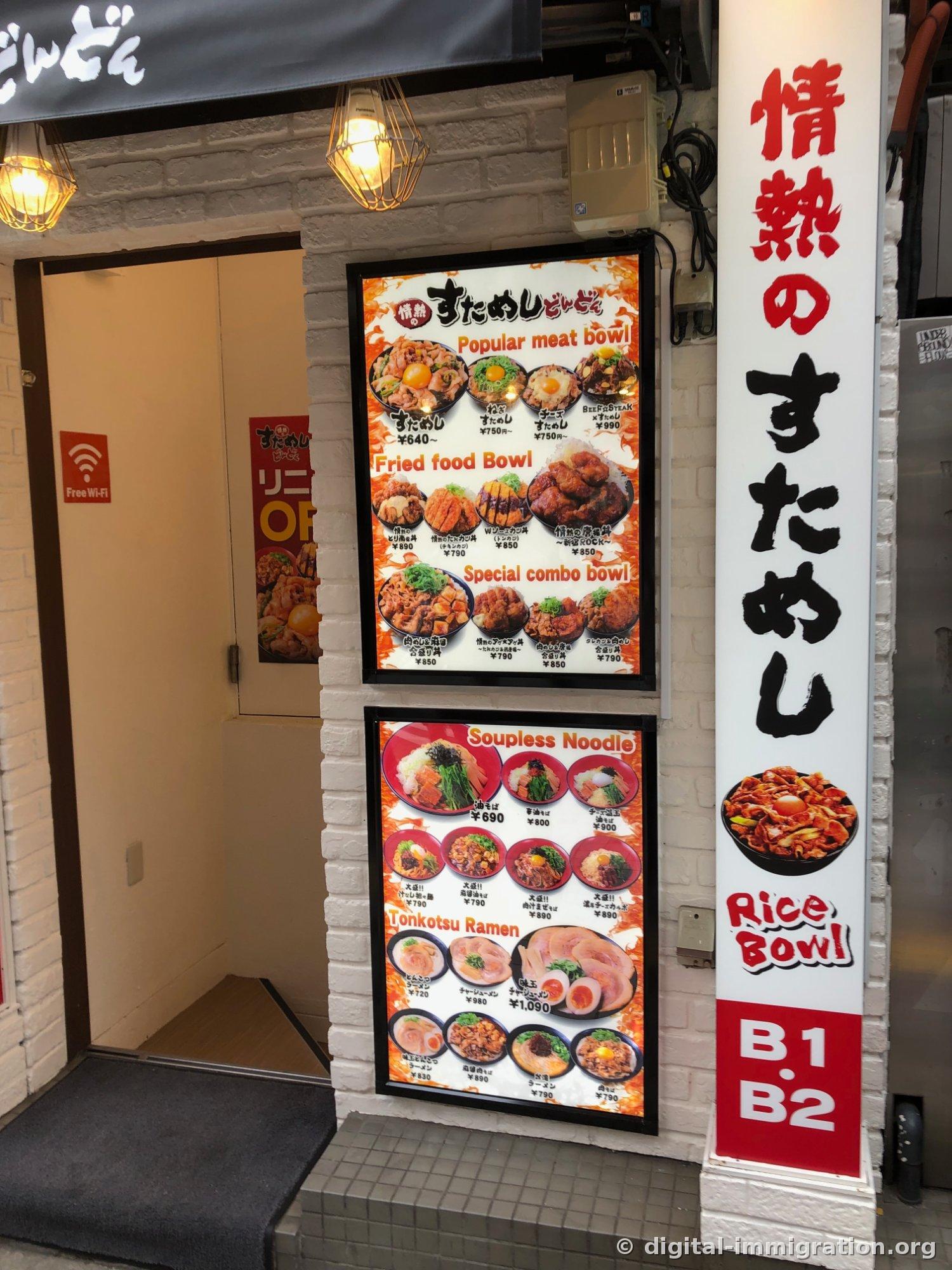Deux panneaux de menu en boîte lumineuse attachés au mur à côté de l'entrée du restaurant, et la marque rouge B1·B2 sur la colonne de droite, avec un autocollant Wi-Fi gratuit visible